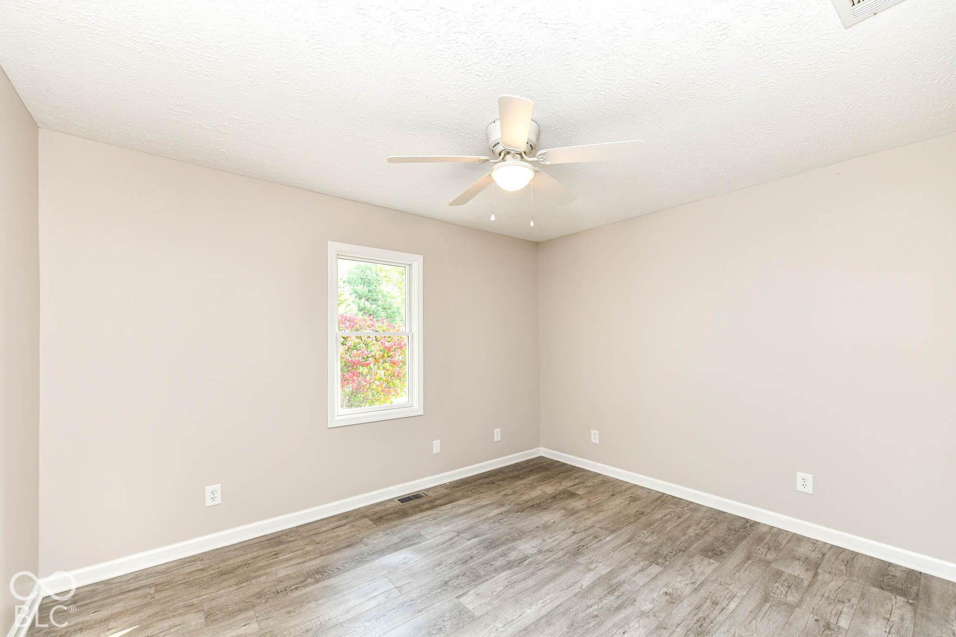 Neutral-toned walls, wood-finish flooring, ceiling fan with integrated lighting, and a white-framed window