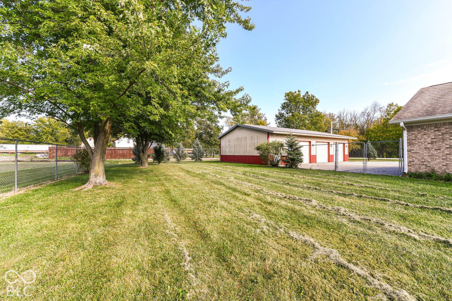 Expansive lot featuring a detached garage with two bays, mature trees, and chain-link fencing