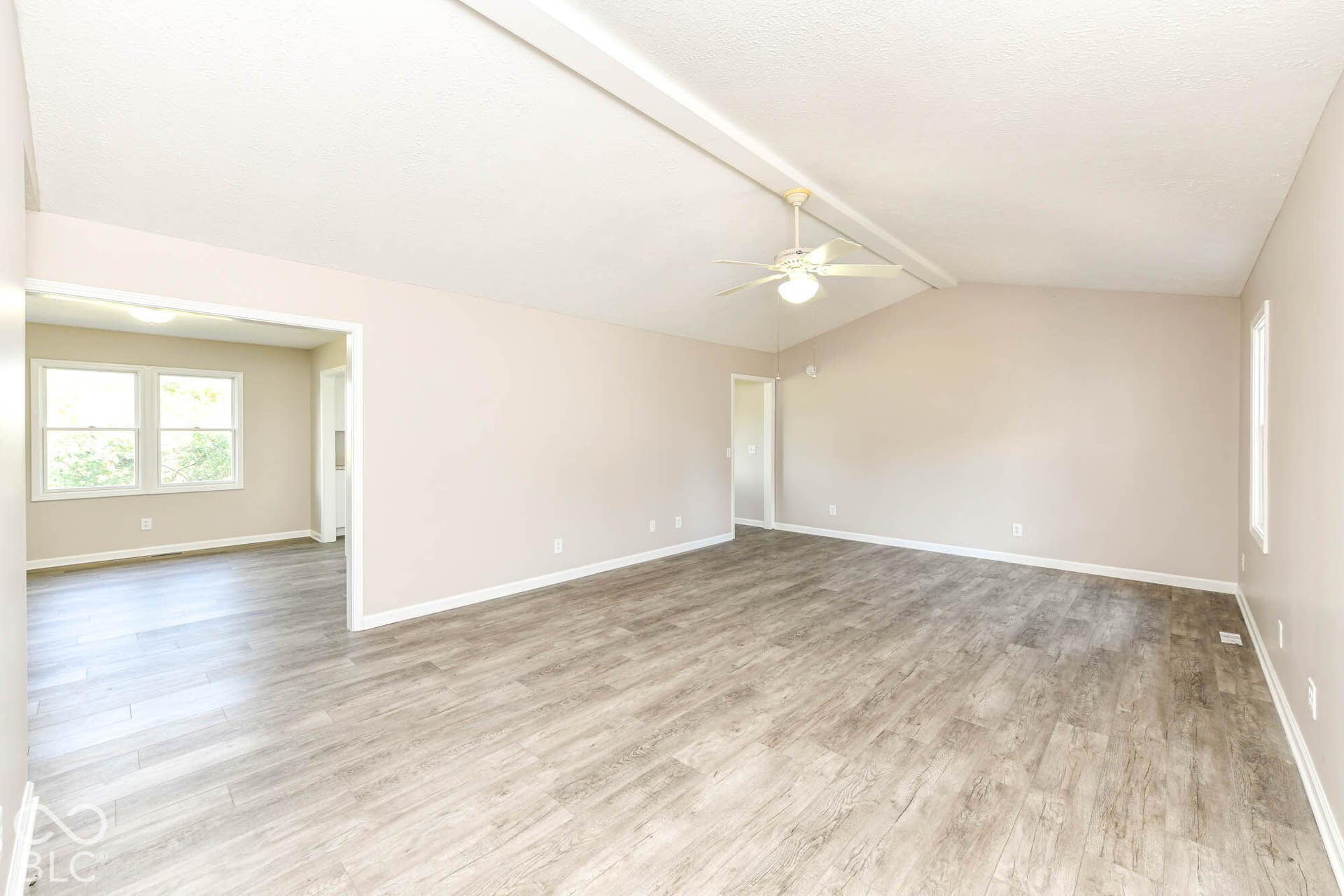 Vaulted ceiling with exposed beam, ceiling fan, wood-finish flooring, and a broad pass-through opening