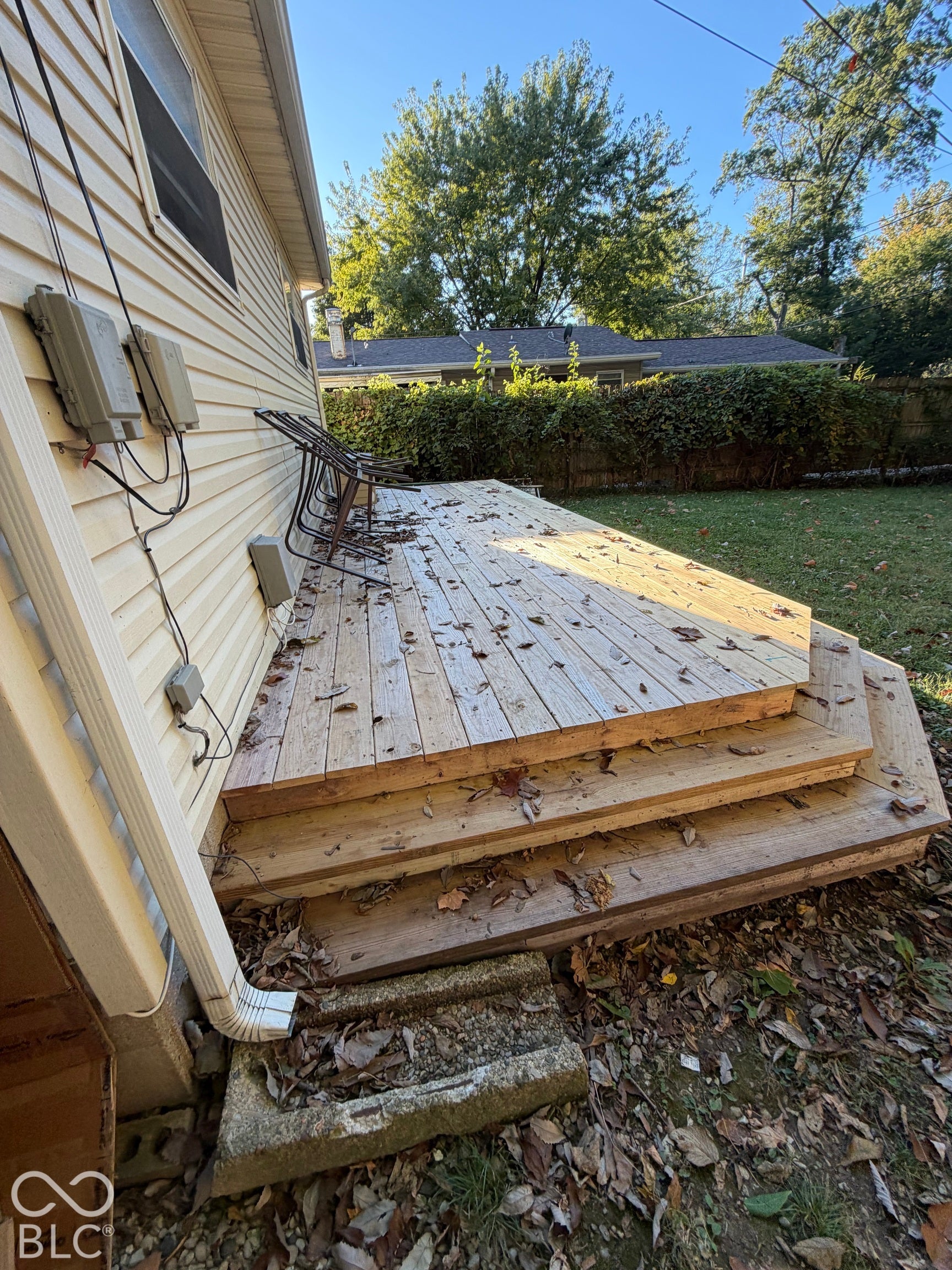 Rear wood deck with multi-level steps, leading to a green lawn with a privacy hedge