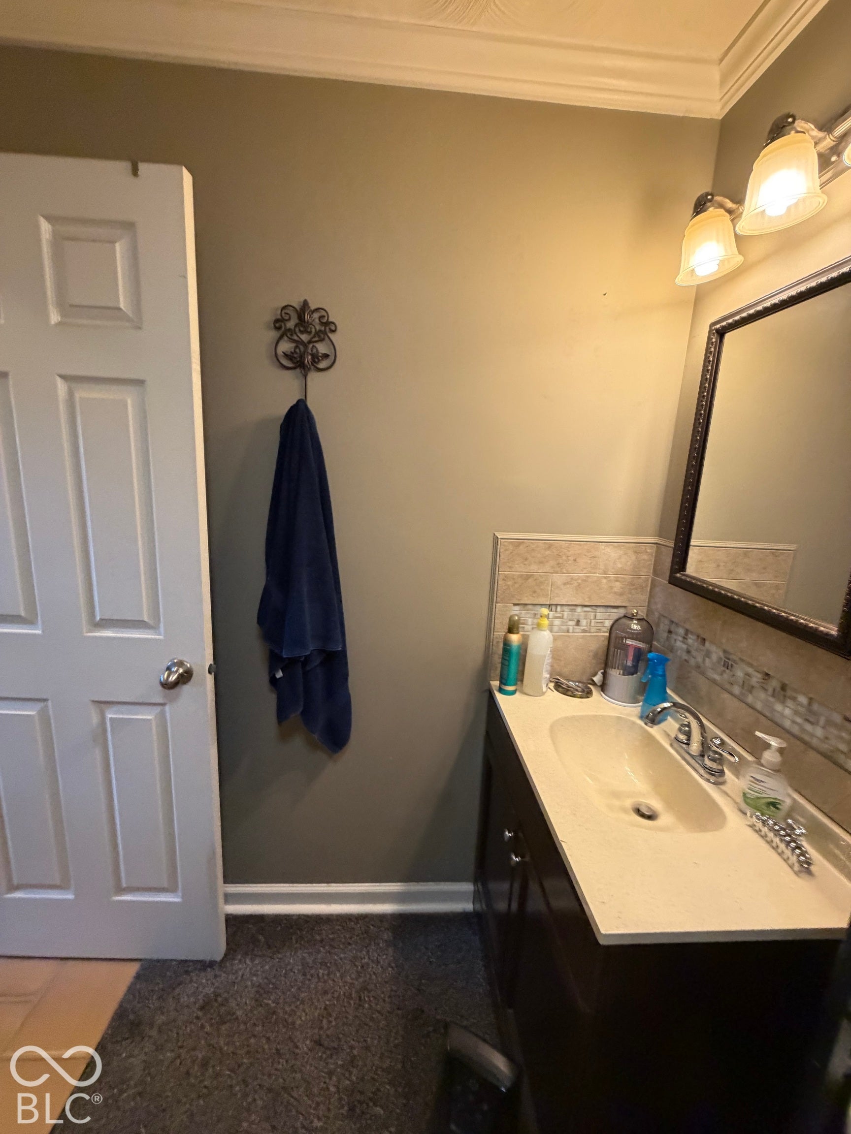 Vanity with integrated sink, wall-mounted lighting, framed mirror, and decorative wall hook