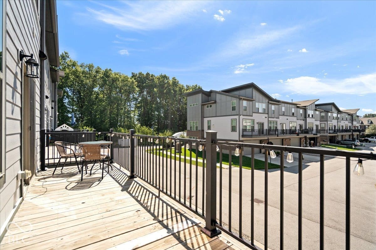 Exterior balcony with wood decking, black metal railings, and attached exterior lighting