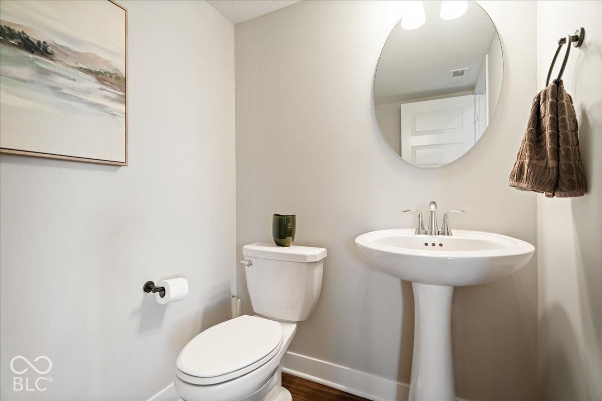 Pedestal sink with chrome-finish faucet, oval mirror, and dark wood-finish flooring
