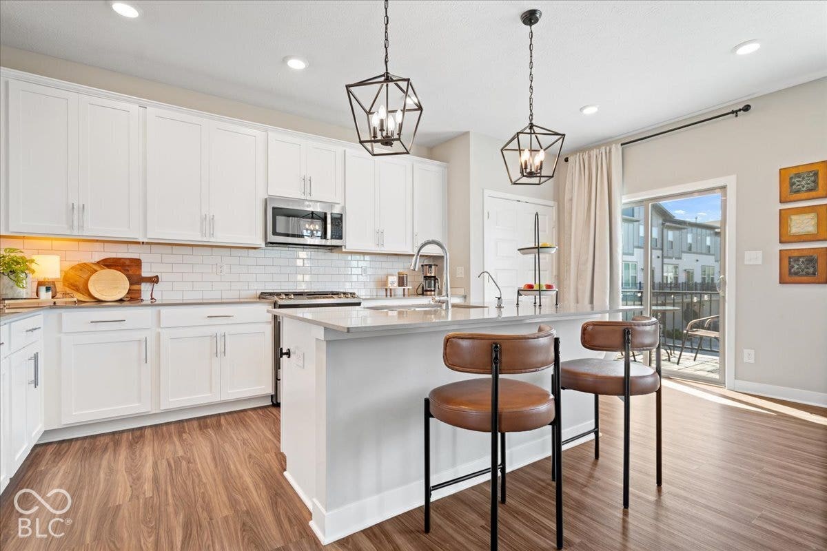 Kitchen featuring white cabinetry, stainless steel appliances, a subway tile backsplash, a center island with a sink, and wood-finish flooring