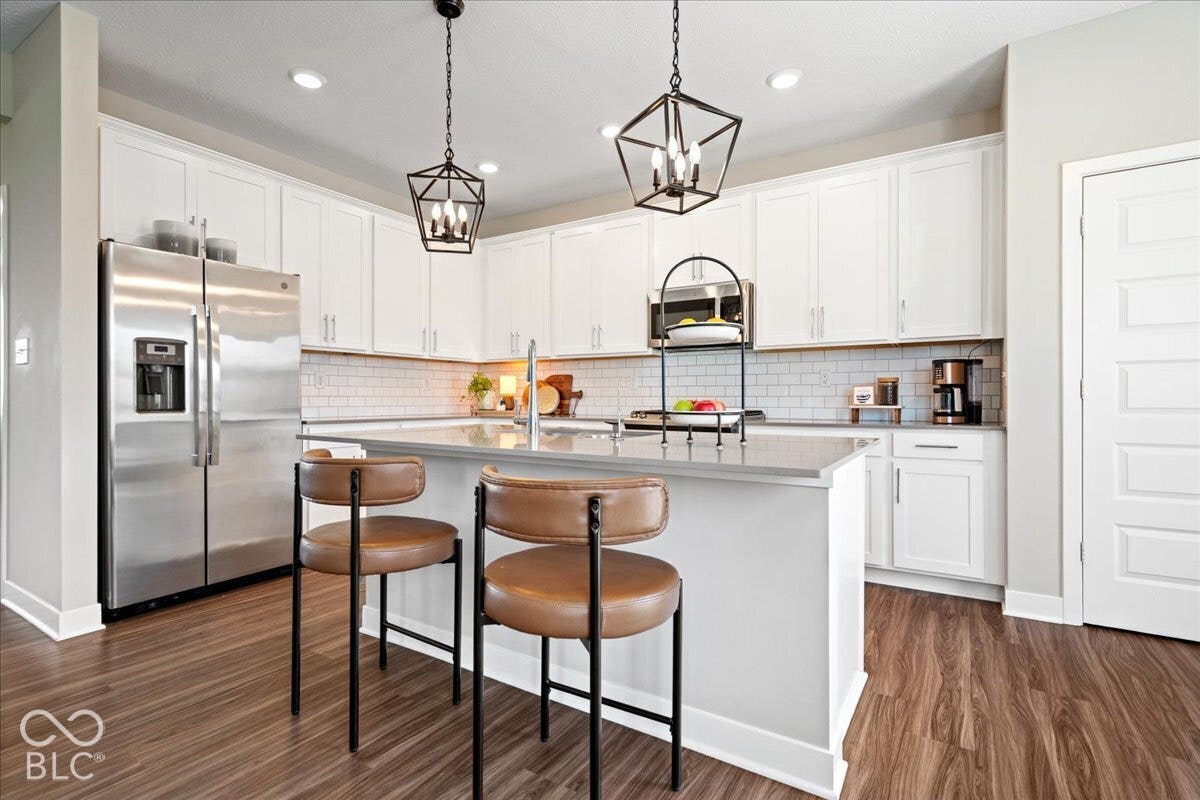 White shaker-style cabinetry, stainless steel appliances, wood-finish flooring, subway tile backsplash, and a kitchen island with seating
