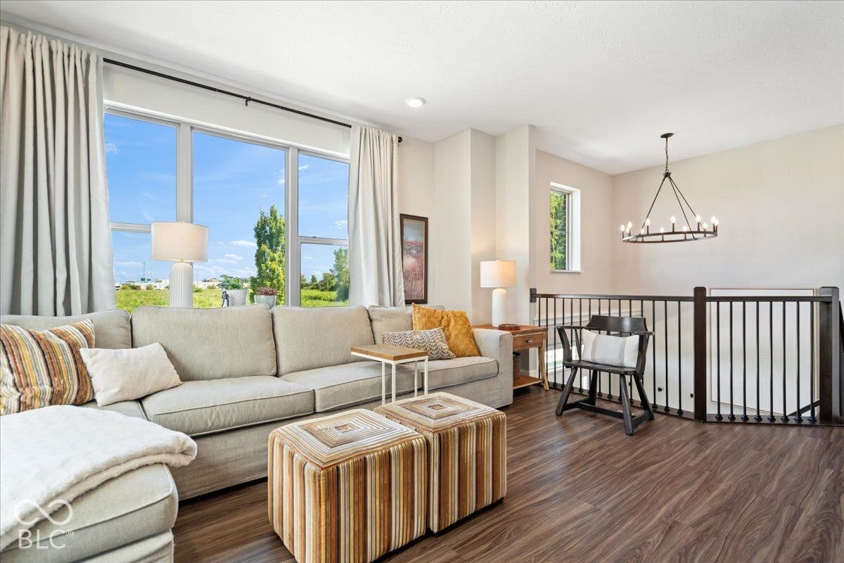 Expansive windows, wood-finish flooring, staircase with dark wood railing, and a wrought iron chandelier