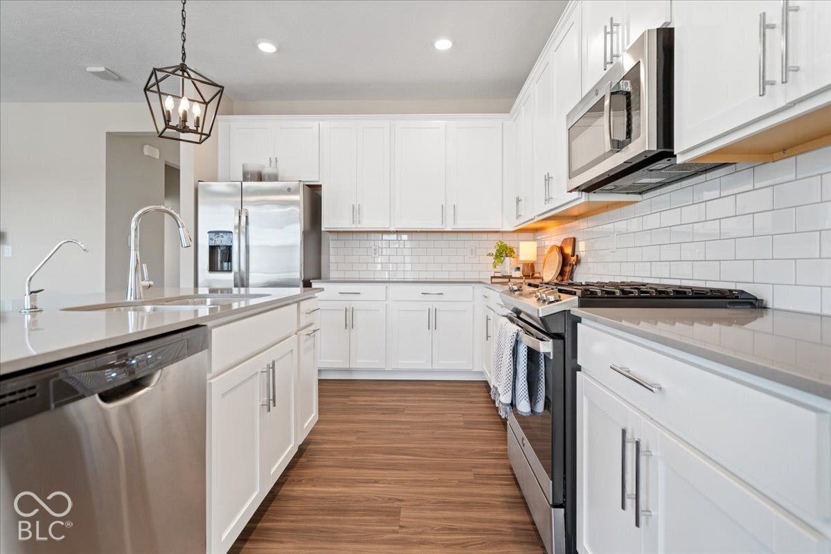 Kitchen featuring white cabinetry, stainless steel appliances, wood-finish flooring, subway tile backsplash, and stone countertops