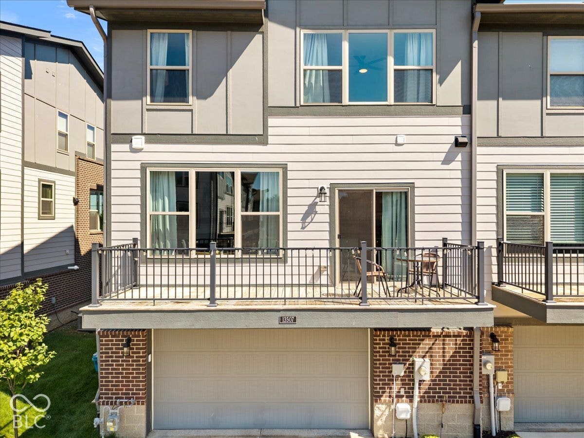 Exterior featuring horizontal siding, a private balcony with metal railings, a sliding glass door, multiple windows, and a garage door