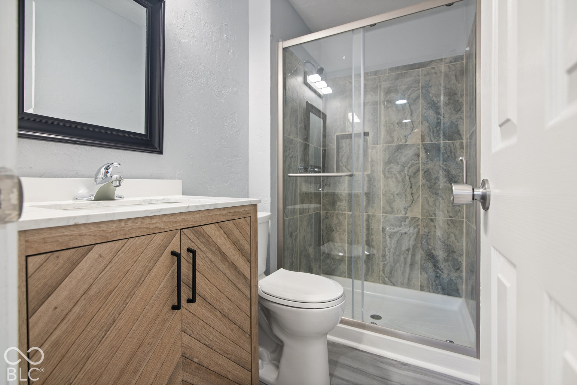 Wood-finish vanity with chevron door detailing, white countertop, and single basin sink