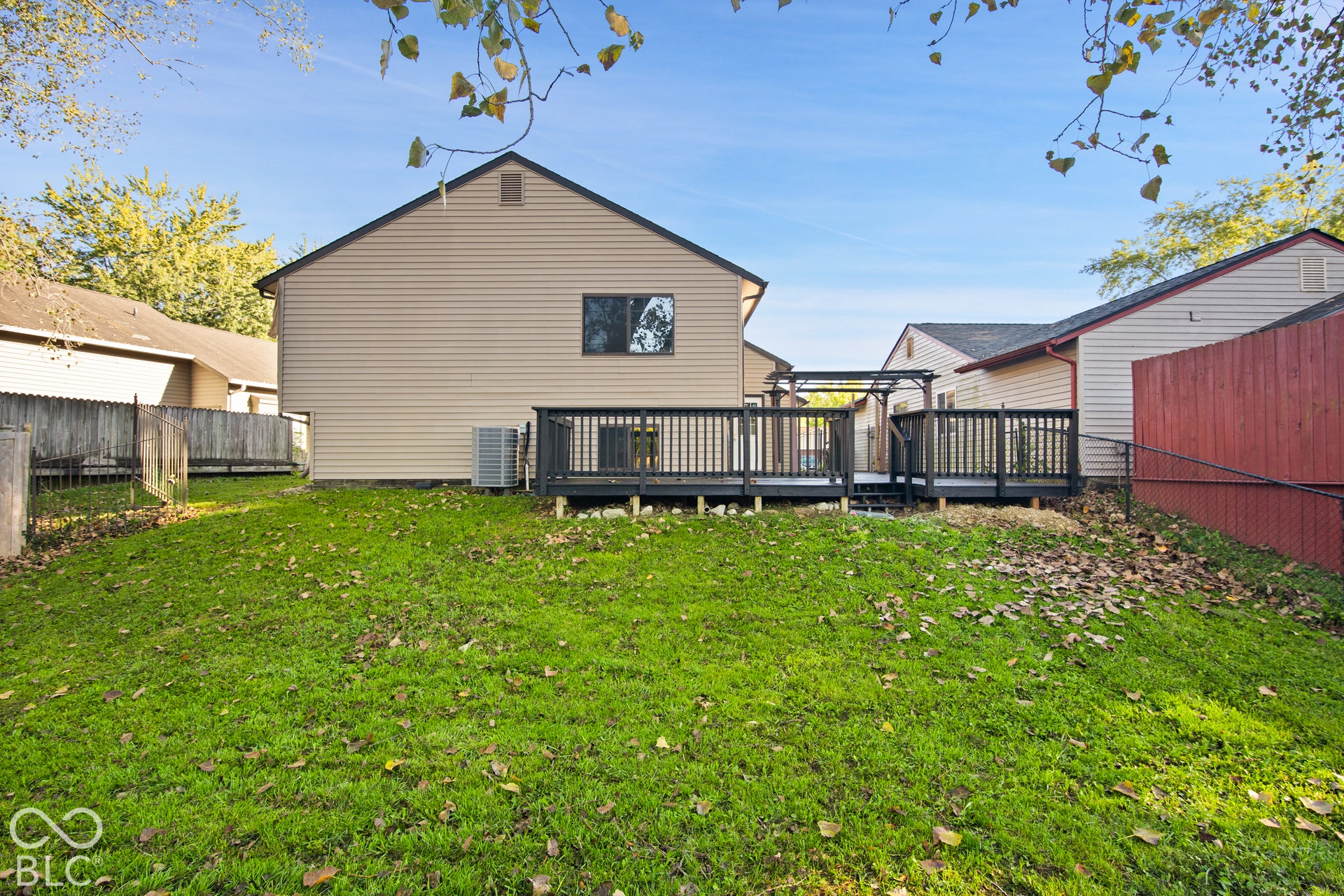 Expansive lawn with a sloped grade, a multi-level deck with dark wood-finish railing, and beige horizontal siding on the main structure