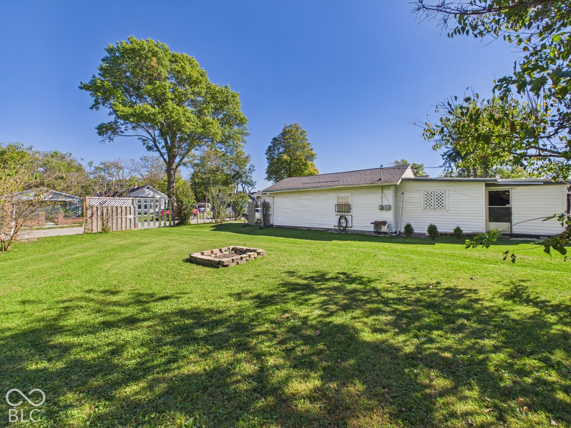 Spacious rear yard with a manicured lawn, established trees, and a stone-edged fire pit