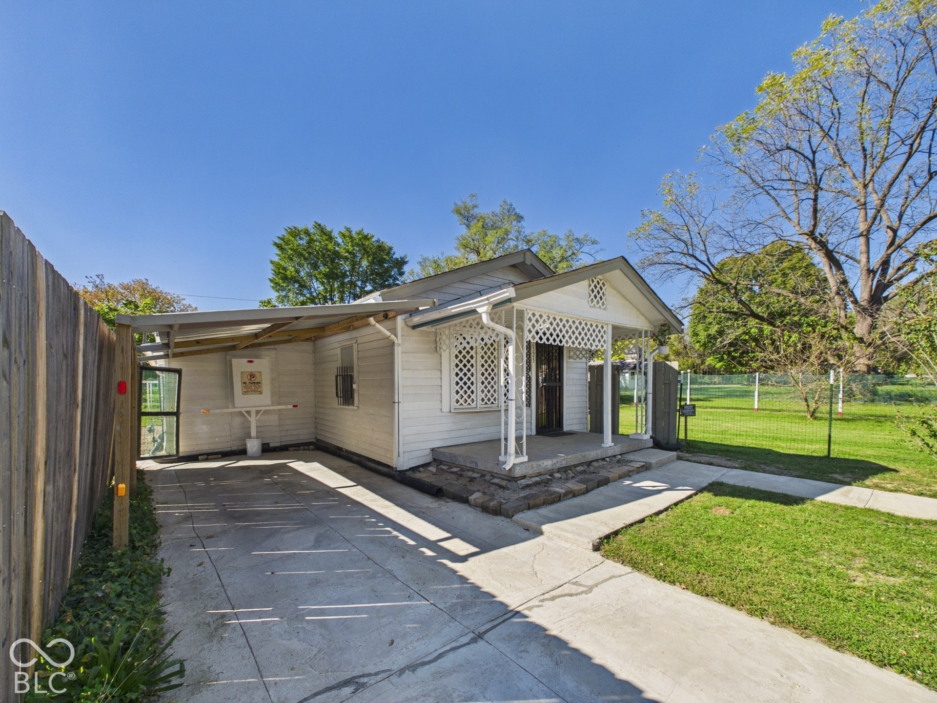 White siding exterior, covered front porch with lattice detailing, concrete walkway, concrete driveway, and a wooden fence