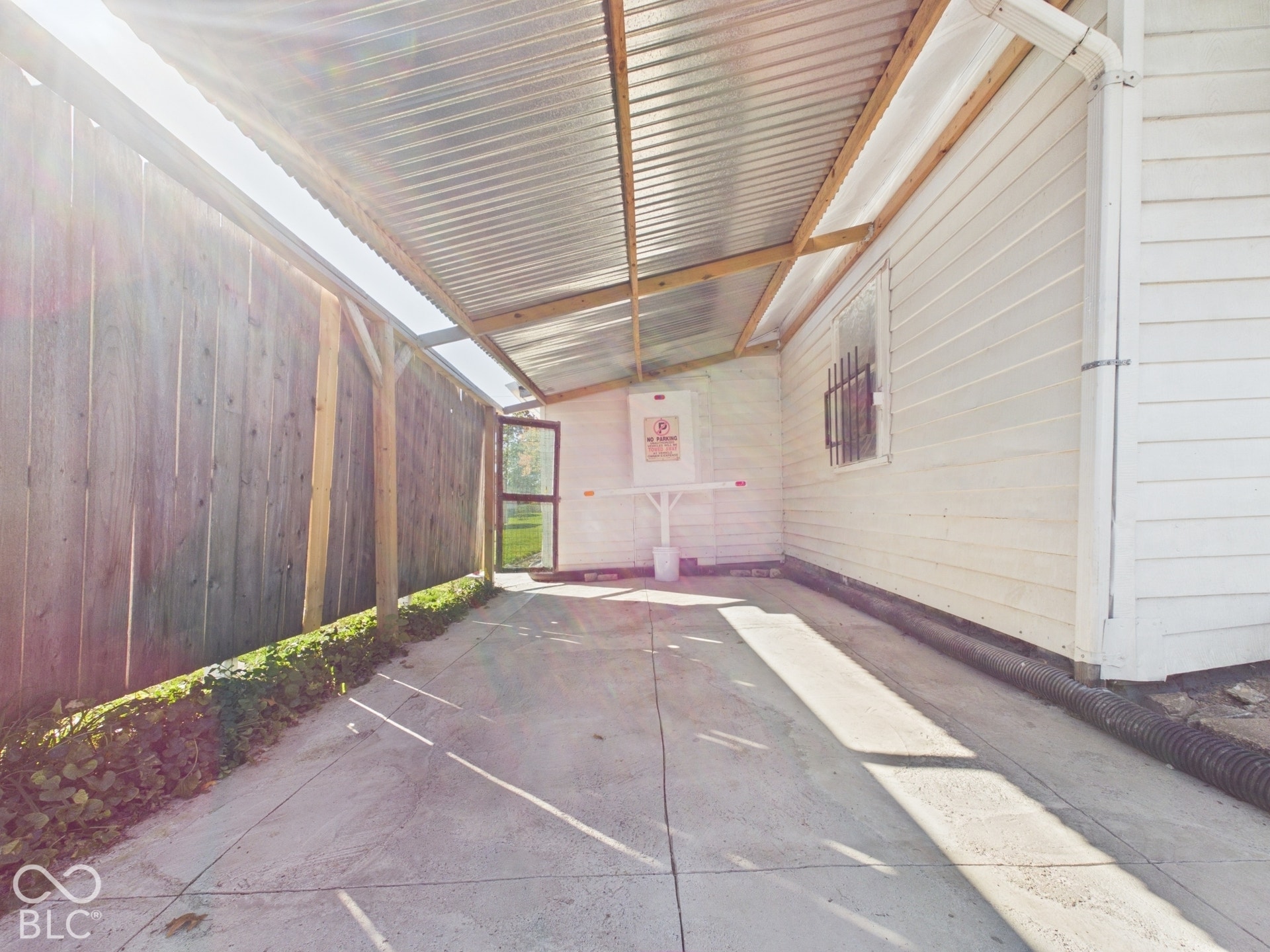 Covered concrete patio featuring a corrugated metal roof, wood support beams, and a wood fence