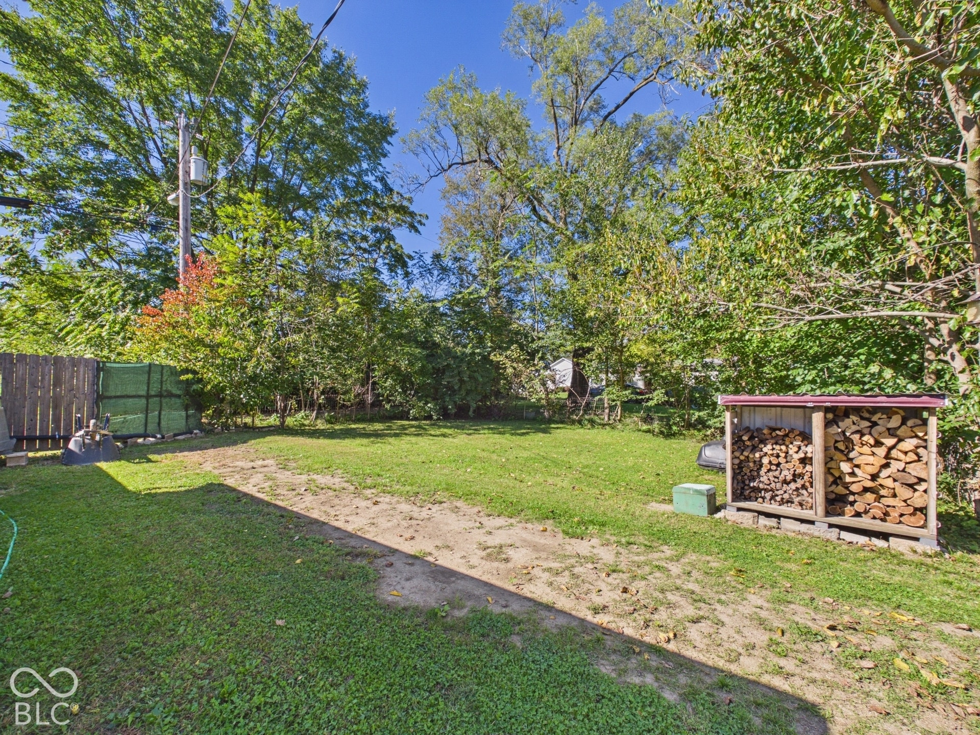 Expansive green lawn with mature perimeter trees, featuring a wood fence, and a firewood storage structure