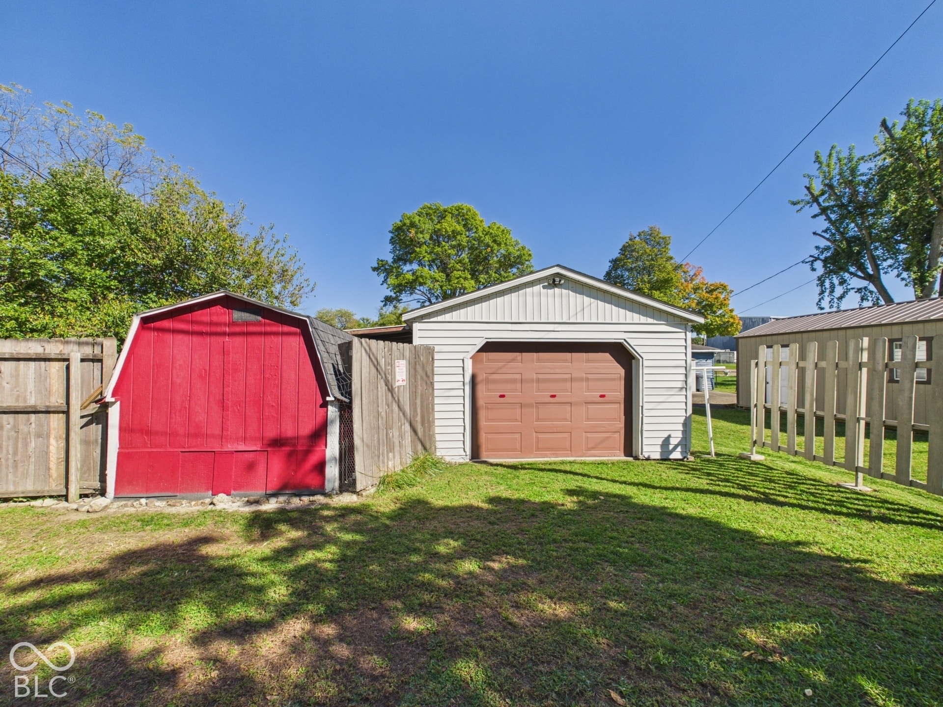 Detached garage with horizontal siding, red barn-style shed, and wooden privacy fence