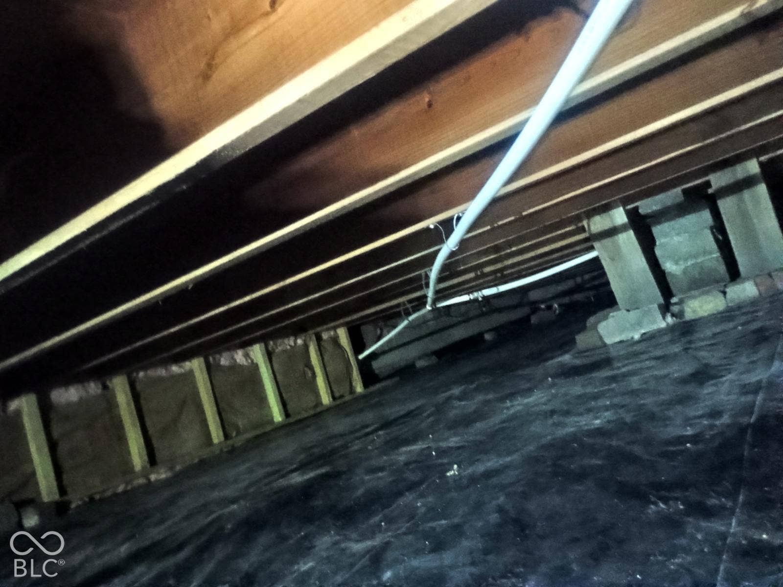 Crawl space featuring visible wood joists, concrete support piers, and a black vapor barrier