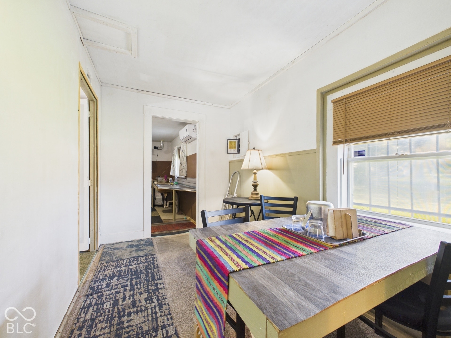 Wood-finish flooring with a durable finish, a window with blind treatments, and a permanent wall-mounted air conditioning unit
