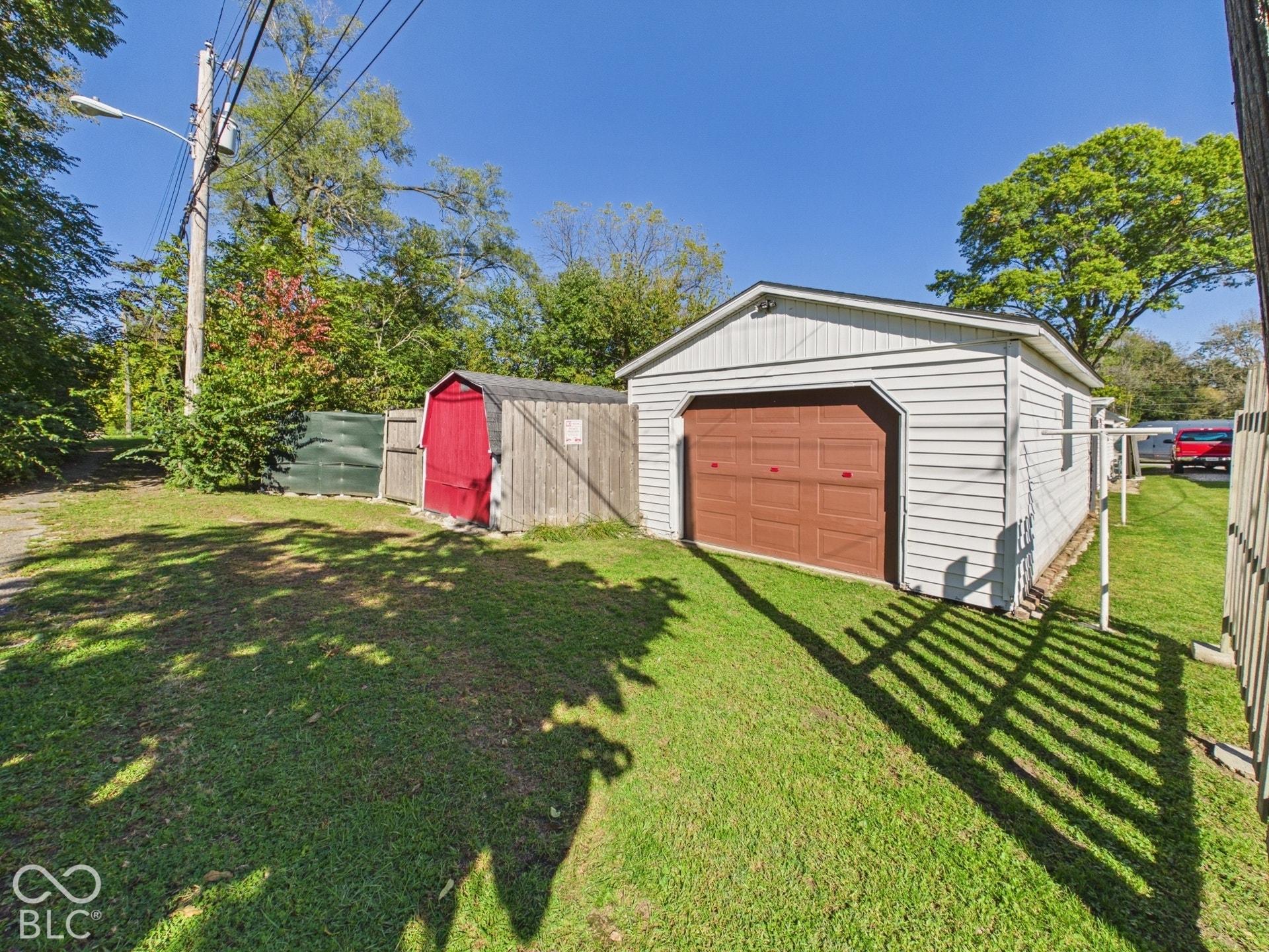 Detached garage with a brown overhead door, a separate red storage shed, and a wooden fence