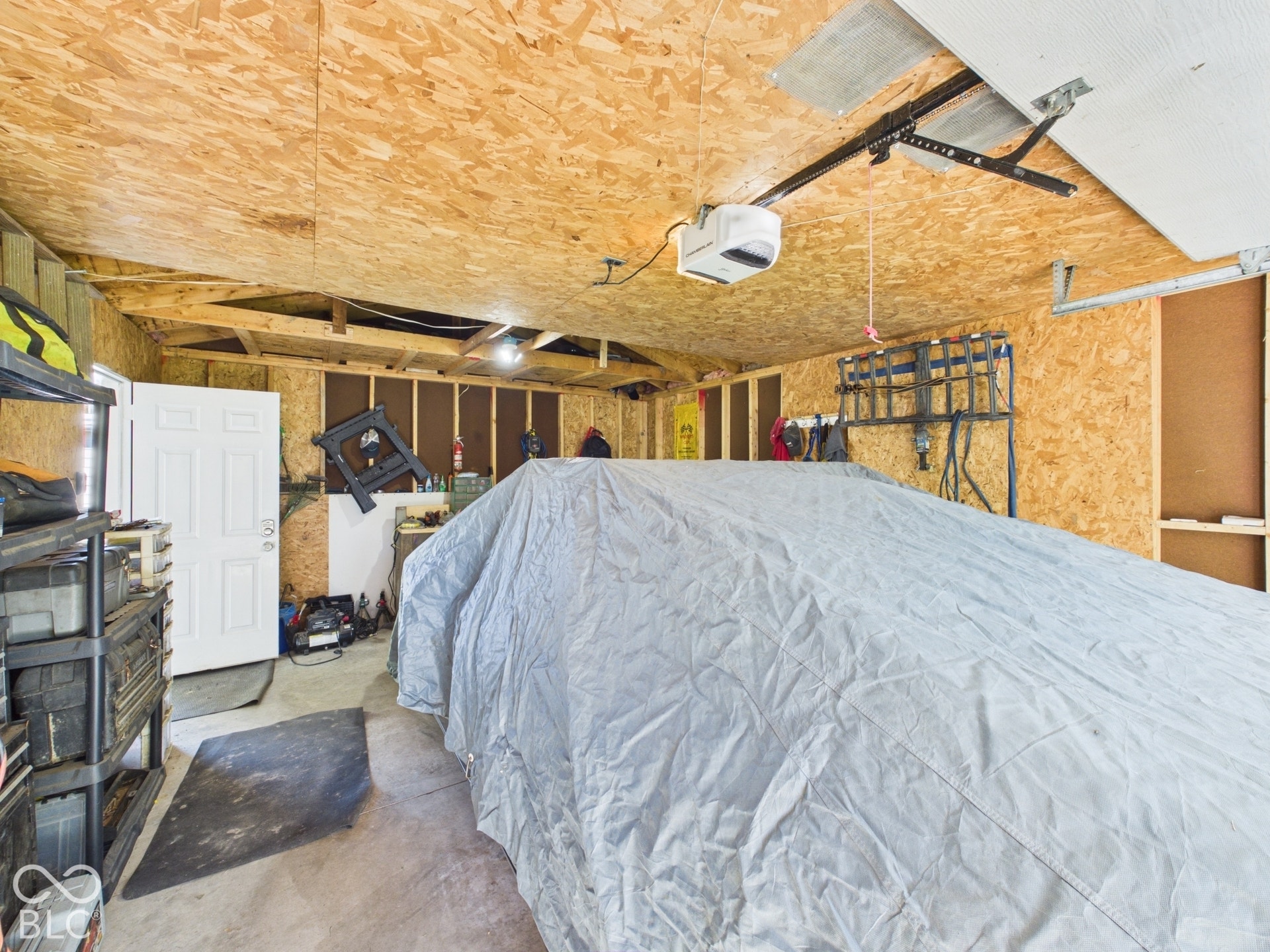 Concrete flooring with a single entry door, exposed wood framing, and wood-panel ceiling