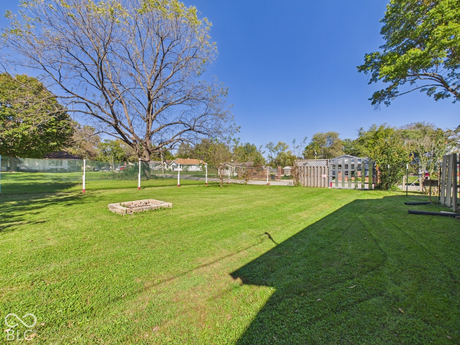 Expansive grassy yard featuring a stone fire pit, mature trees, and a wood fence