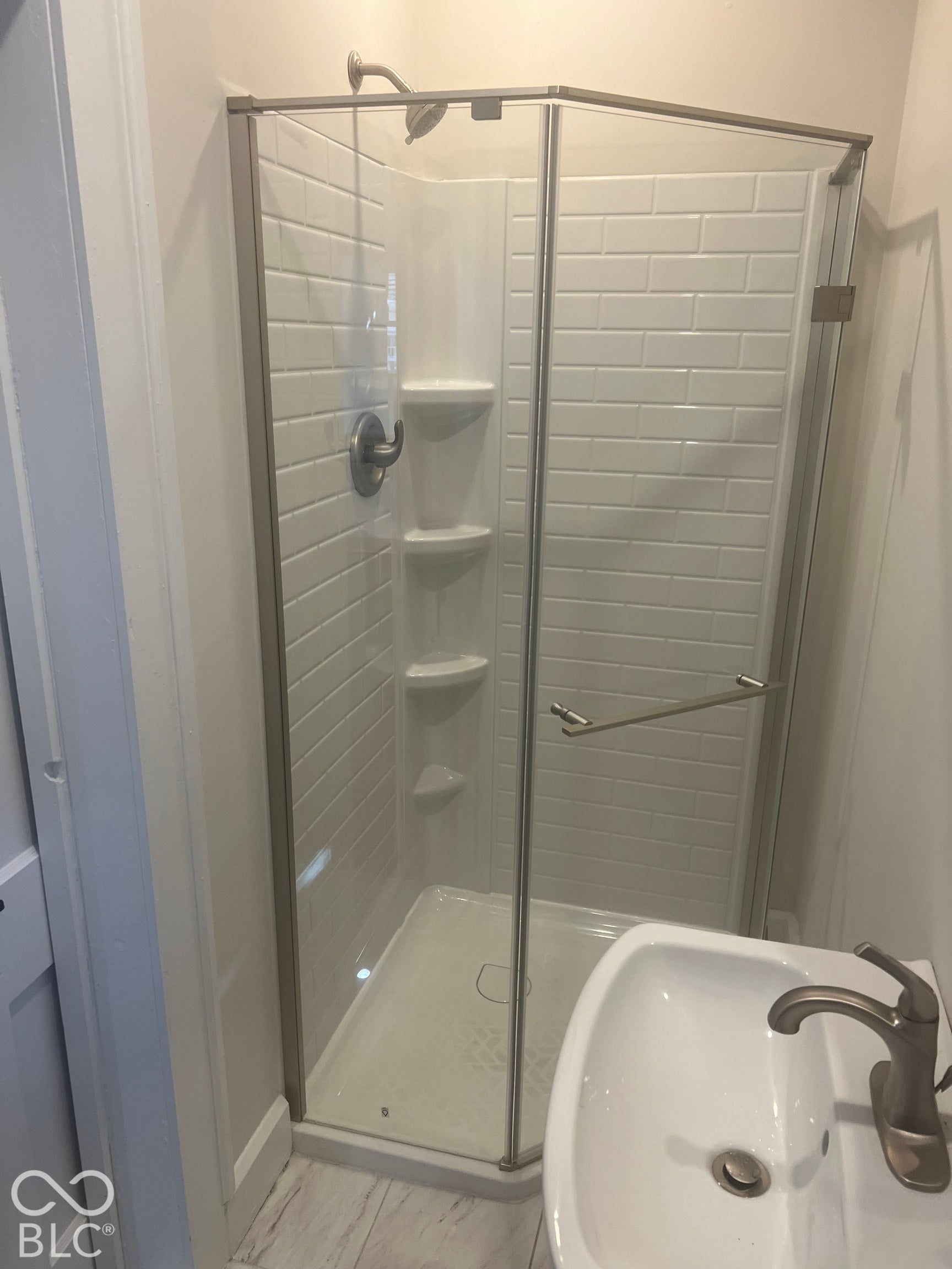 Corner shower with glass enclosure, subway tile surround, built-in shelving, and a wall-mounted shower head