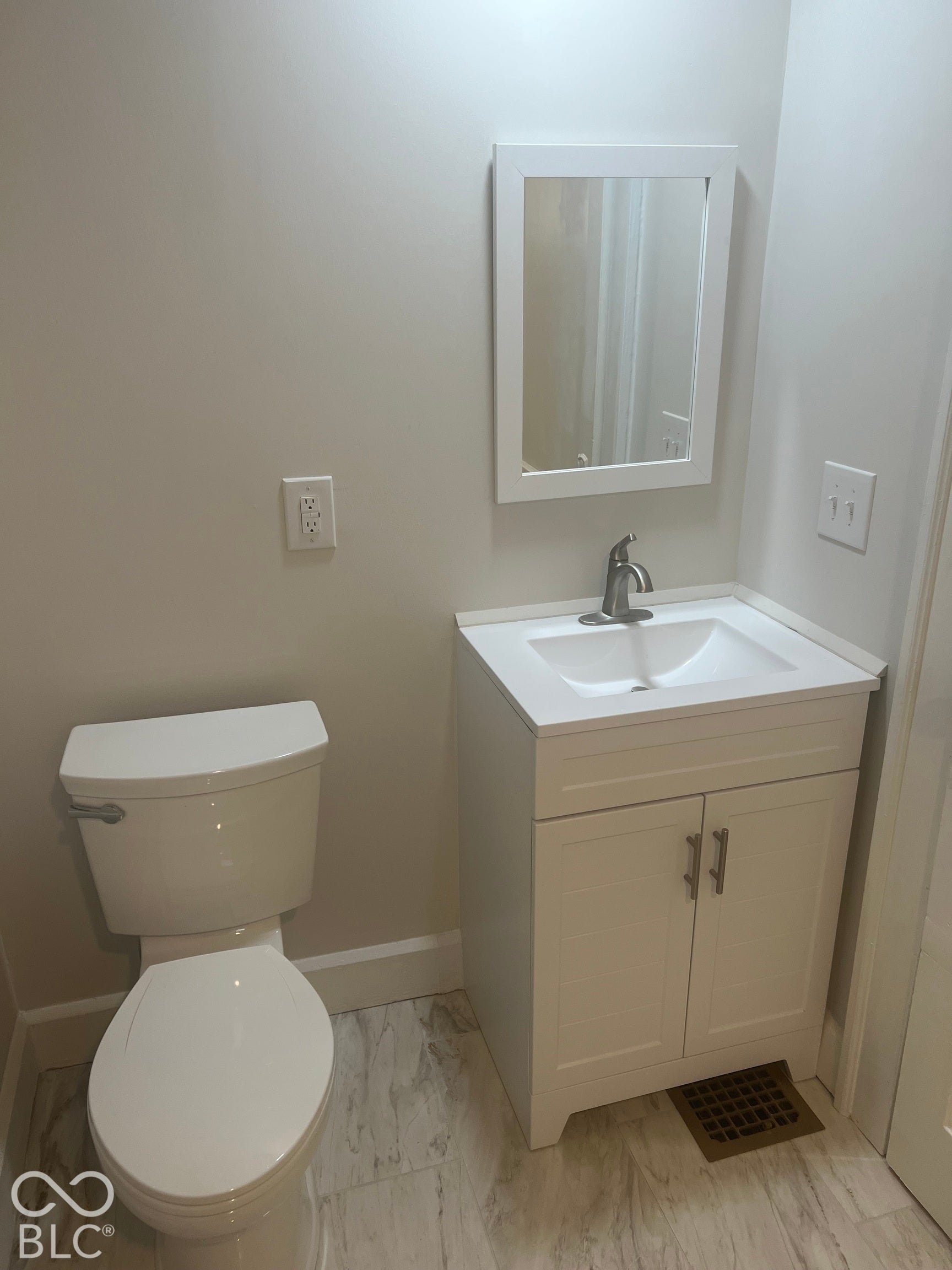 White vanity with an integrated sink and brushed nickel faucet, framed mirror, and tile flooring