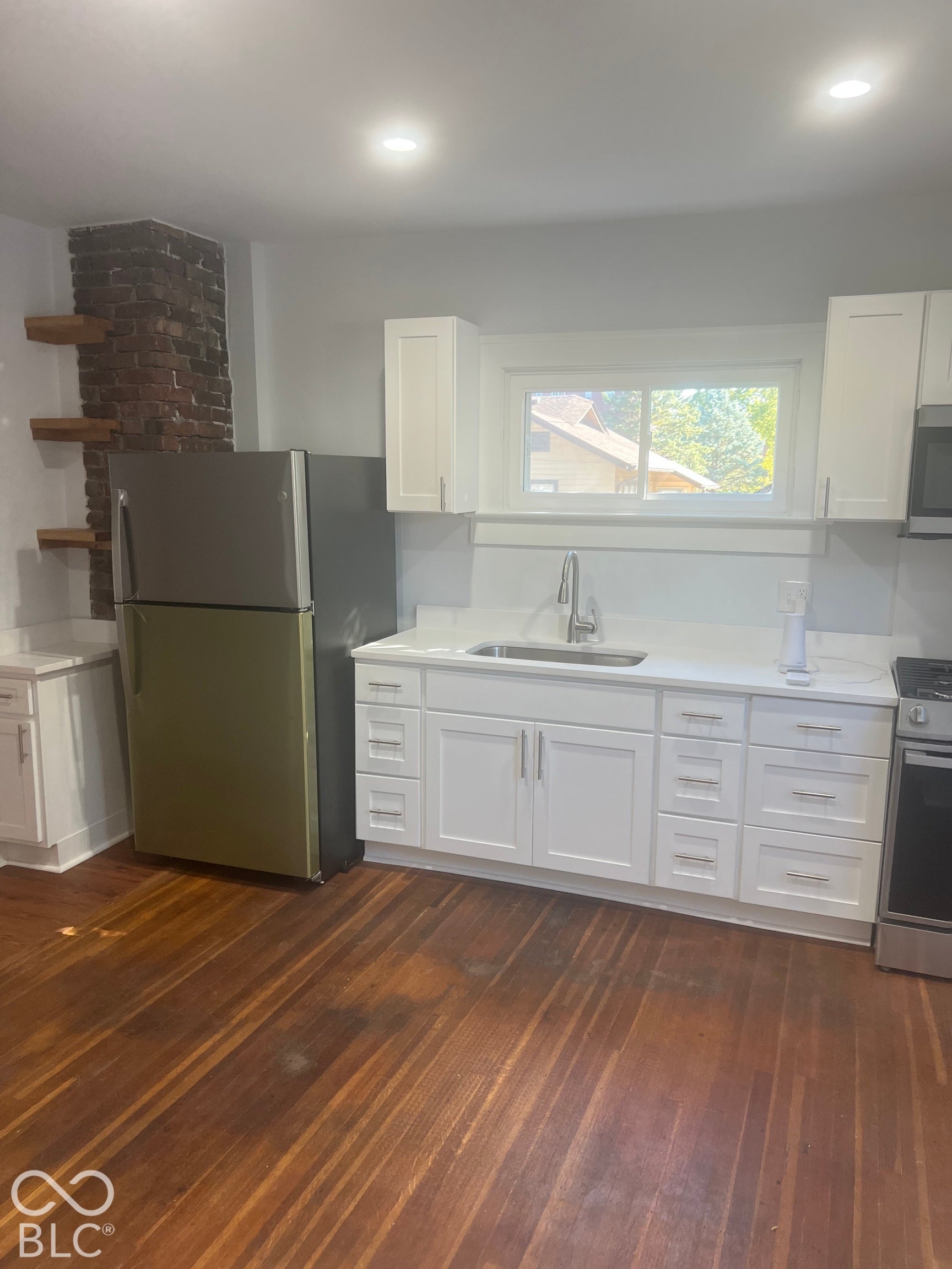 Kitchen featuring wood-finish flooring, white cabinetry, a stainless steel sink, and a refrigerator