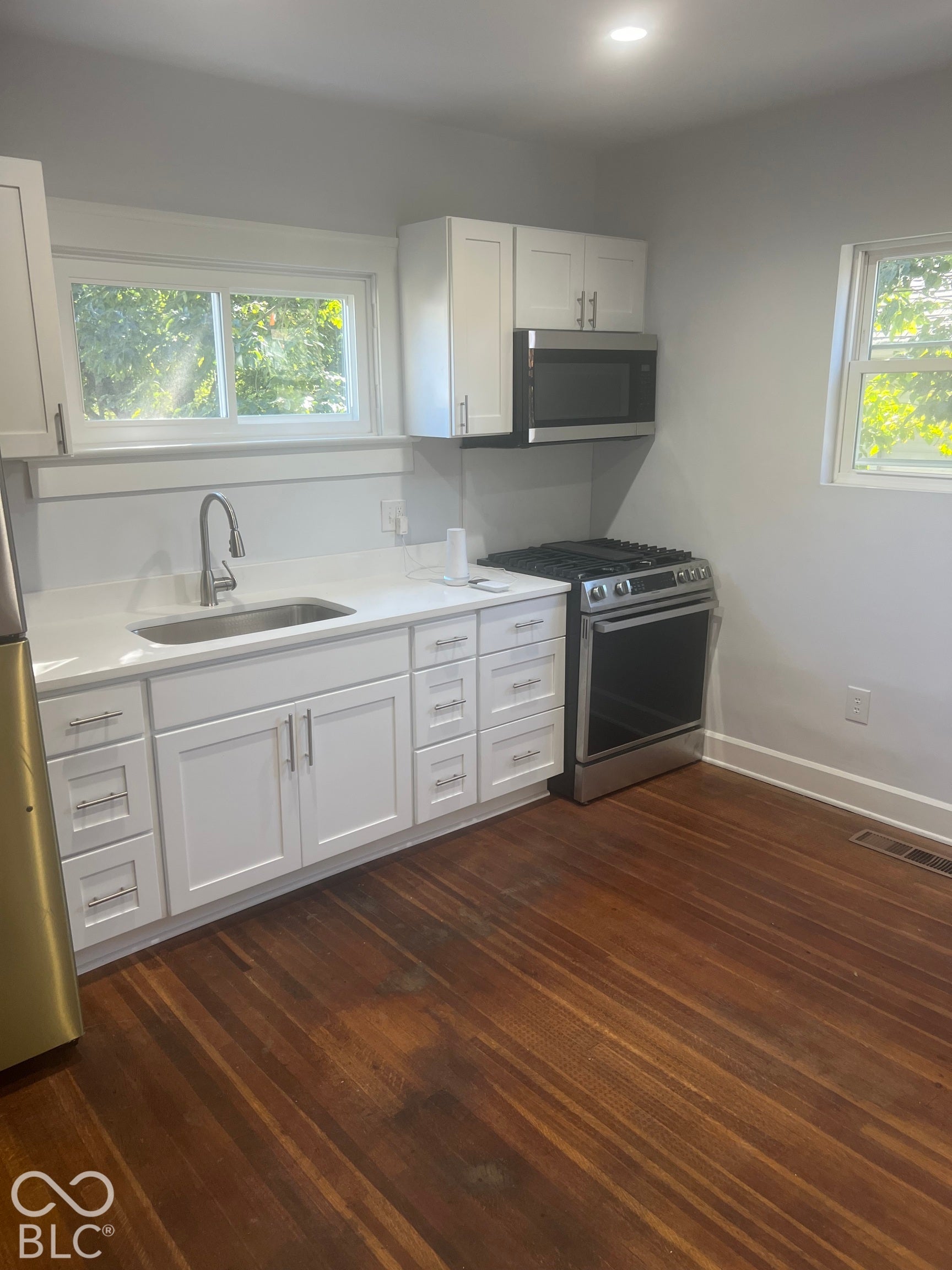 White cabinetry with stainless steel hardware, stainless steel appliances, light-toned countertops, and wood-finish flooring