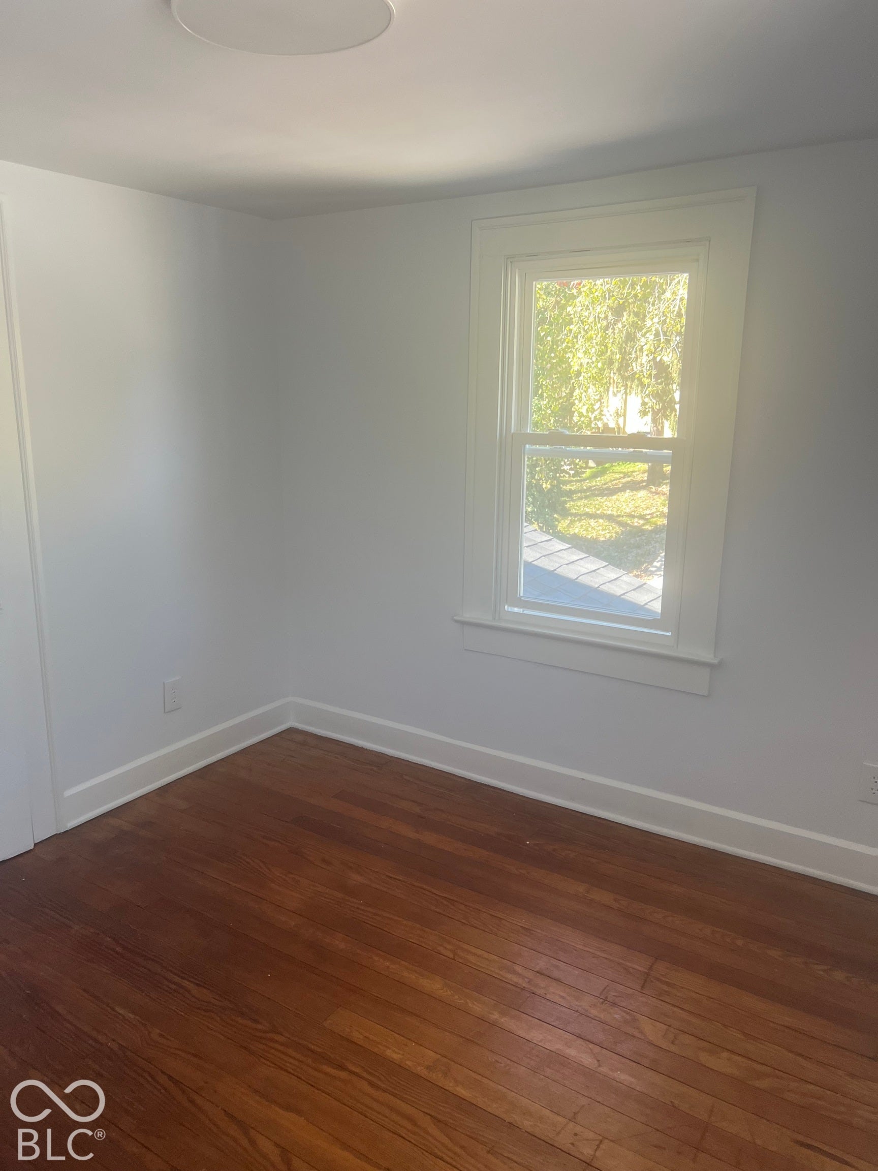 Hardwood flooring, white painted walls, window with trim, ceiling-mounted light fixture, white baseboards
