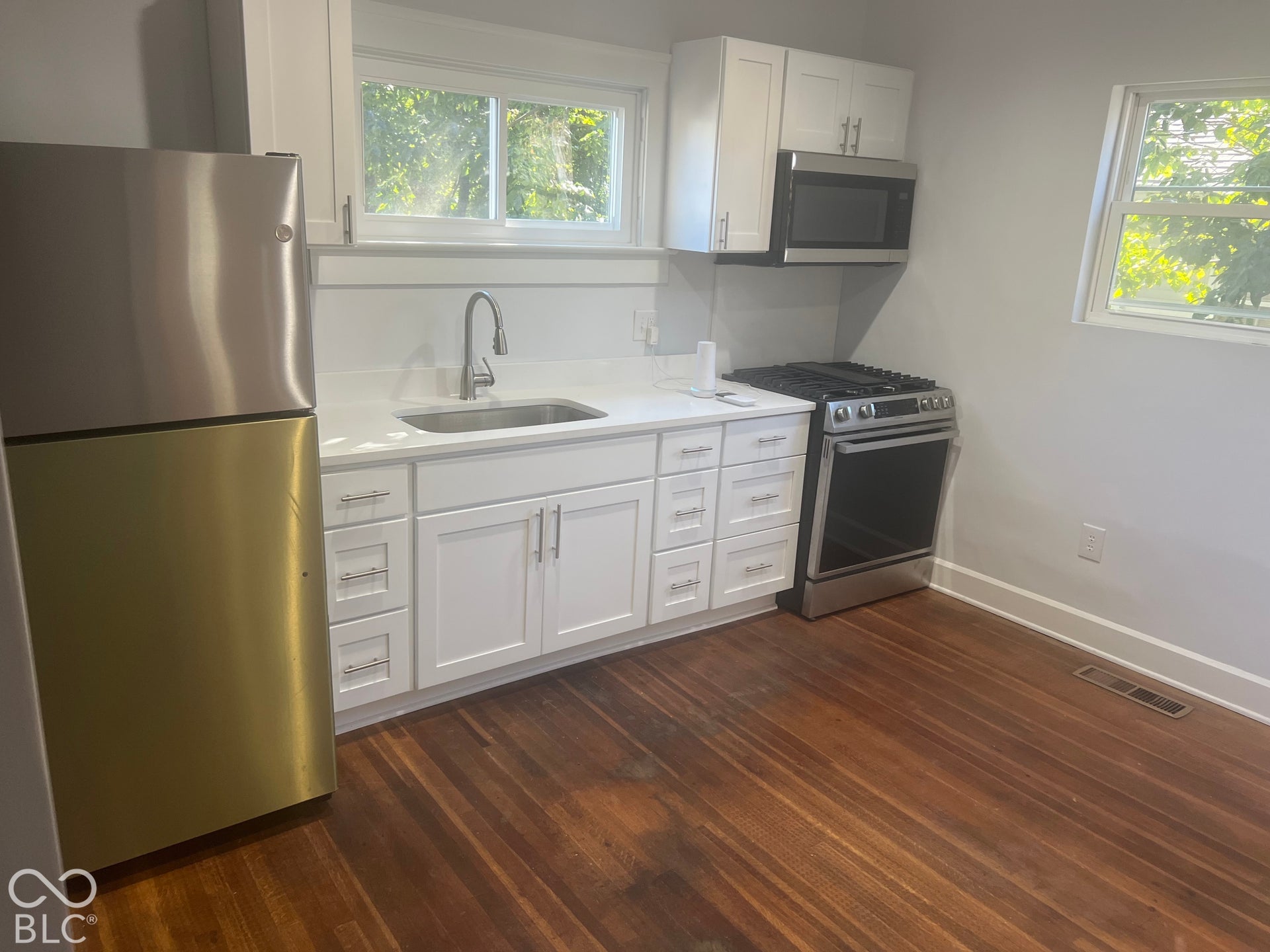 White shaker-style cabinetry with stainless steel hardware, stainless steel appliances, light-toned countertops, and wood-finish flooring