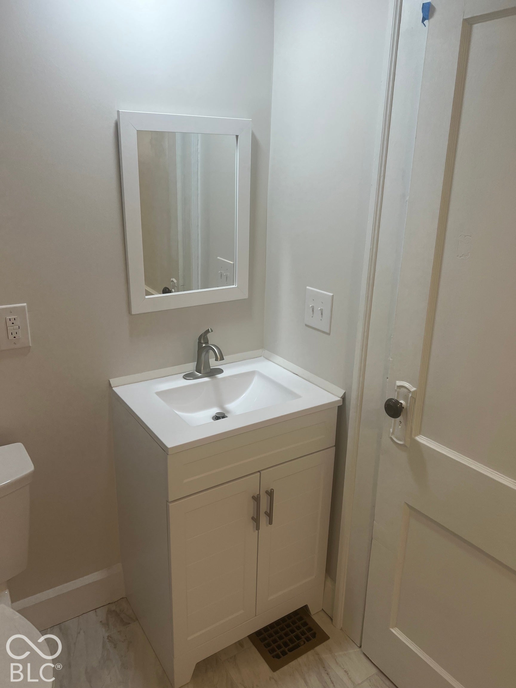 White vanity with an integrated sink and brushed nickel faucet, framed mirror, and tile flooring