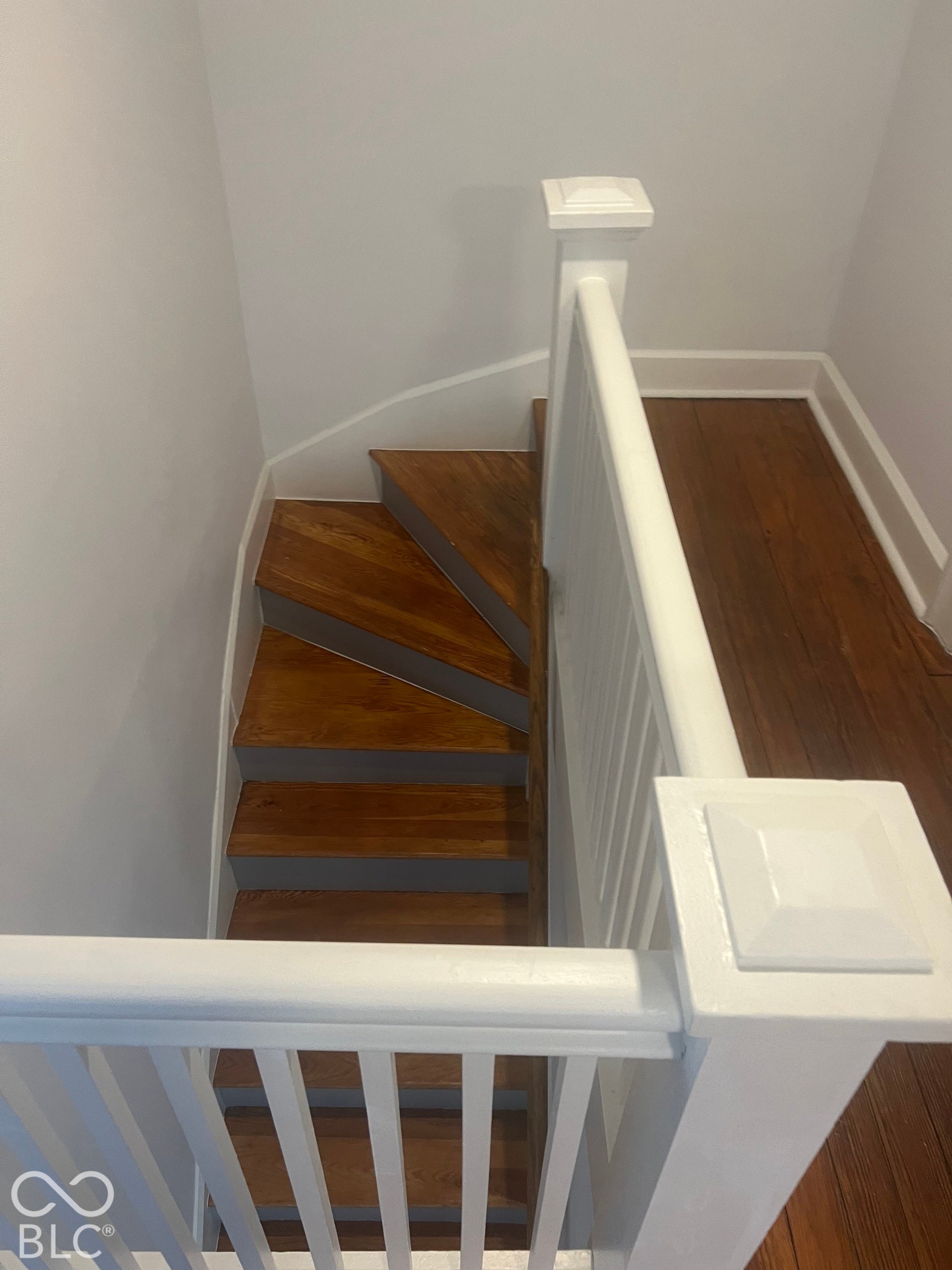 Staircase featuring wood-finish treads, white risers, and a white painted balustrade