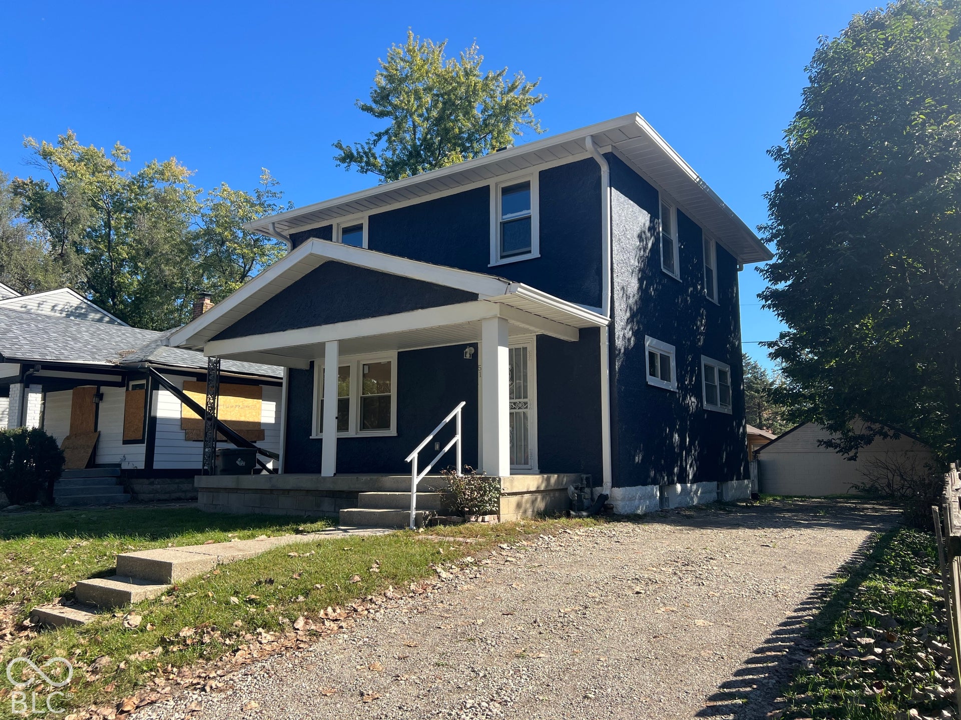 Two-story residence featuring a covered front porch, white porch columns, dark siding, and a gravel driveway