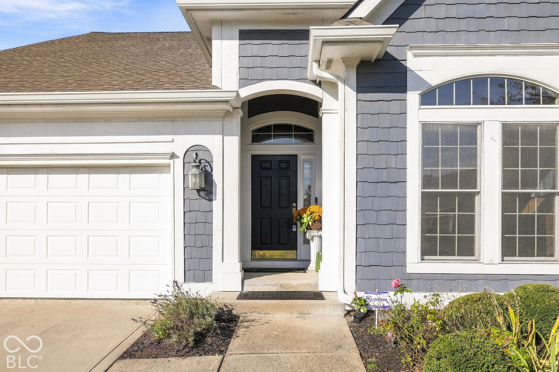 Exterior facade featuring dark grey shake siding, white trim, an arched entryway, a six-panel door with a transom window, and an attached multi-car garage