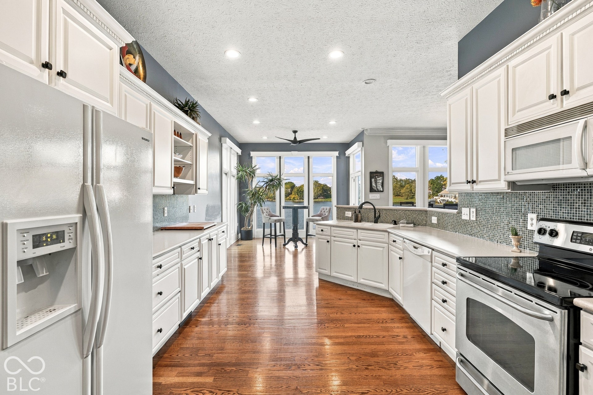 Kitchen featuring white cabinetry, wood-finish flooring, mosaic tile backsplash, recessed lighting, and stainless steel appliances