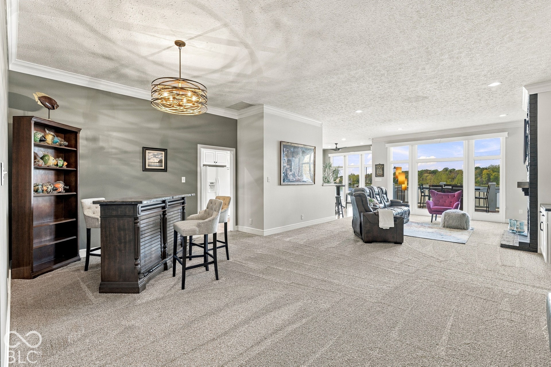 Open-concept living space featuring a built-in wet bar, crown molding, a circular tiered pendant light, carpeted flooring, and a floor-to-ceiling multi-panel window configuration