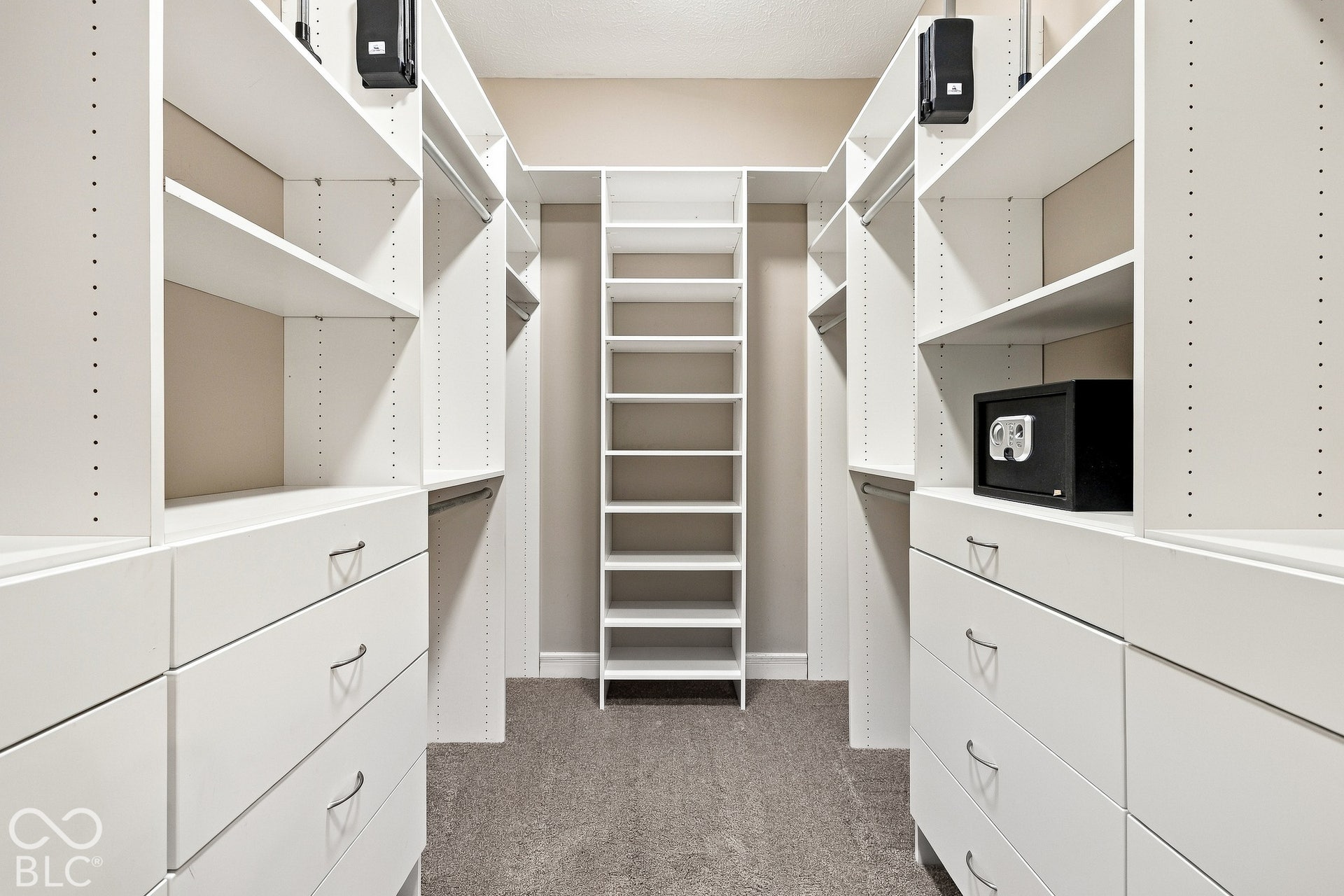 Walk-in closet featuring white built-in shelving, integrated storage drawers with silver-tone hardware, and carpeting