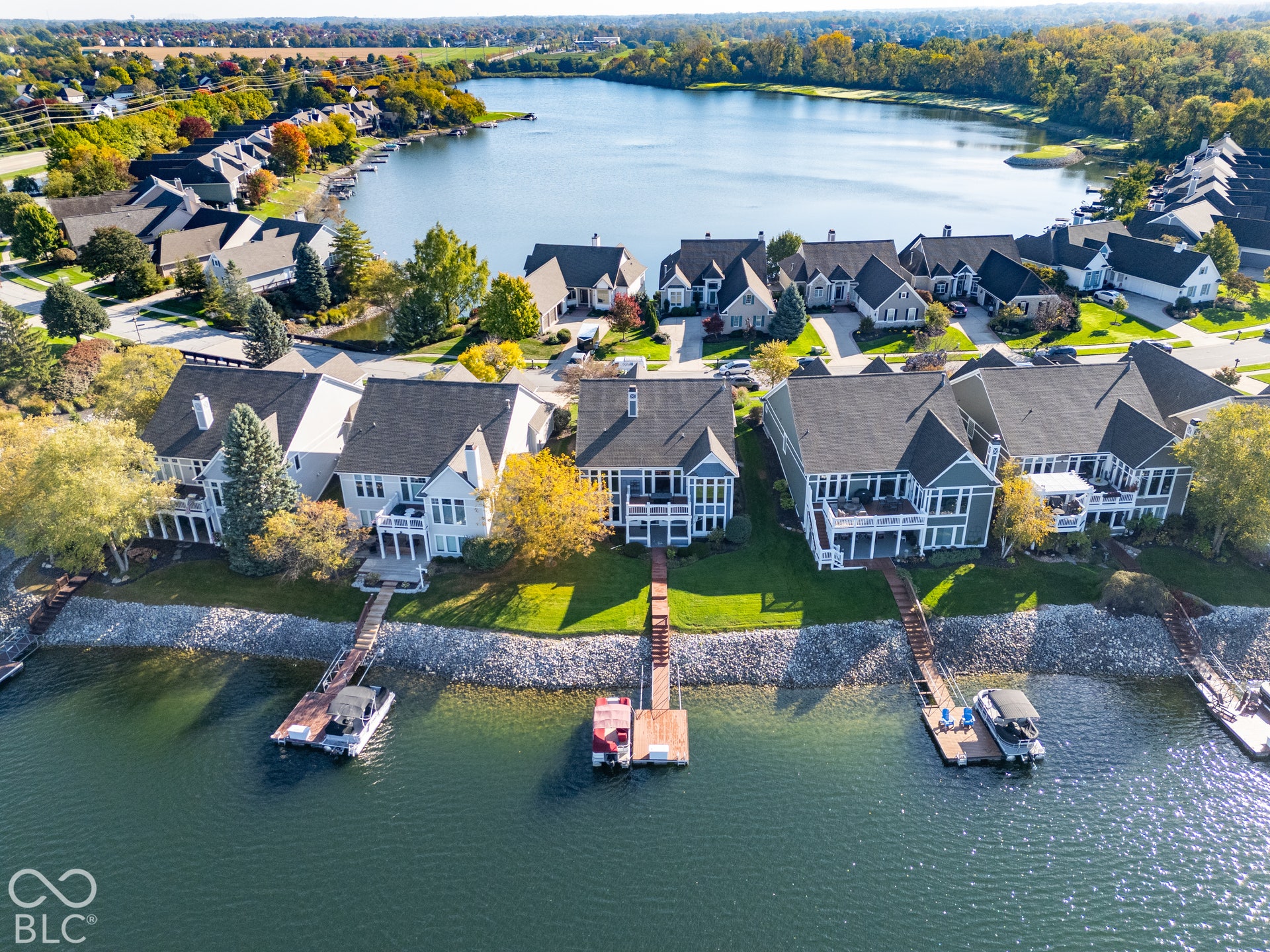 Waterfront residential properties featuring private wooden docks, multi-level decks, manicured lawns, and stone-reinforced shorelines