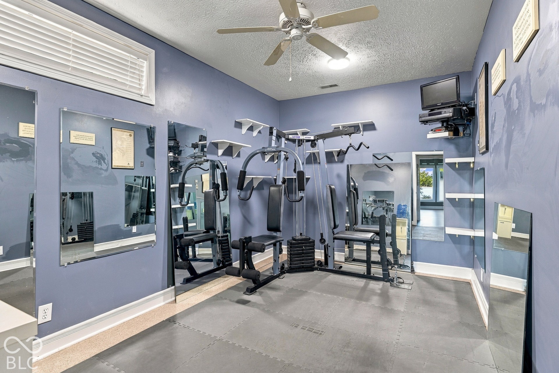 Room featuring wall-to-wall mirror panels, multiple fixed shelving units, a white ceiling fan with integrated lighting, and modular floor surfacing