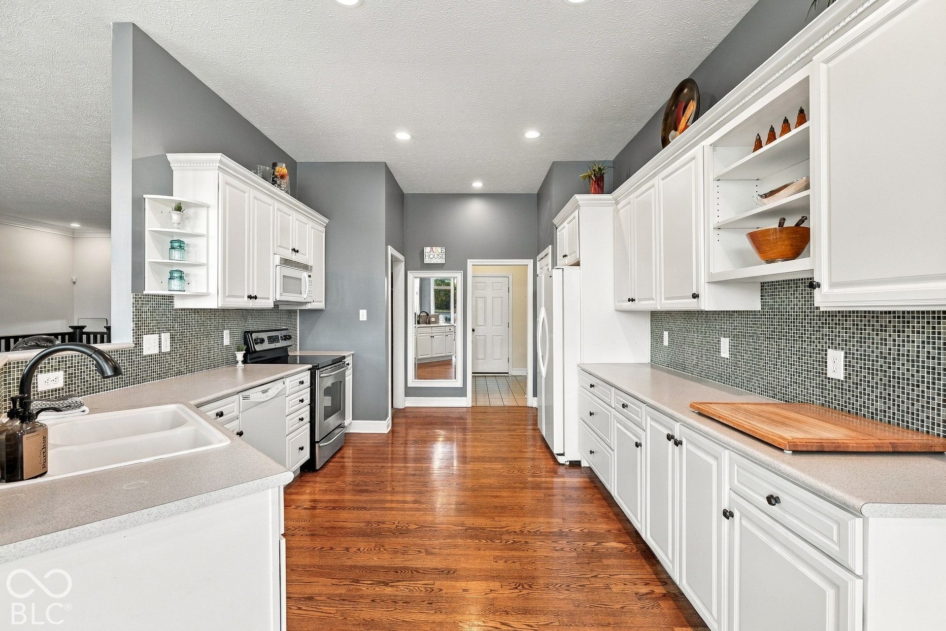 Kitchen featuring white cabinetry, wood-finish flooring, mosaic tile backsplash, solid-surface countertops, and recessed lighting