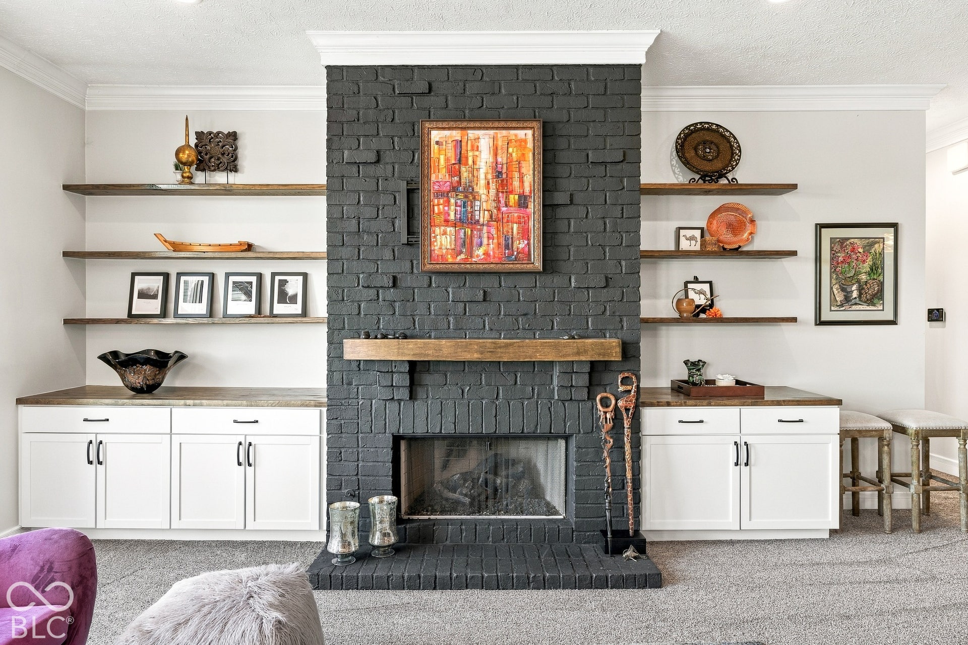 Floor-to-ceiling painted brick fireplace featuring a wood mantel, flanked by built-in lower cabinetry with wood countertops and custom floating shelving