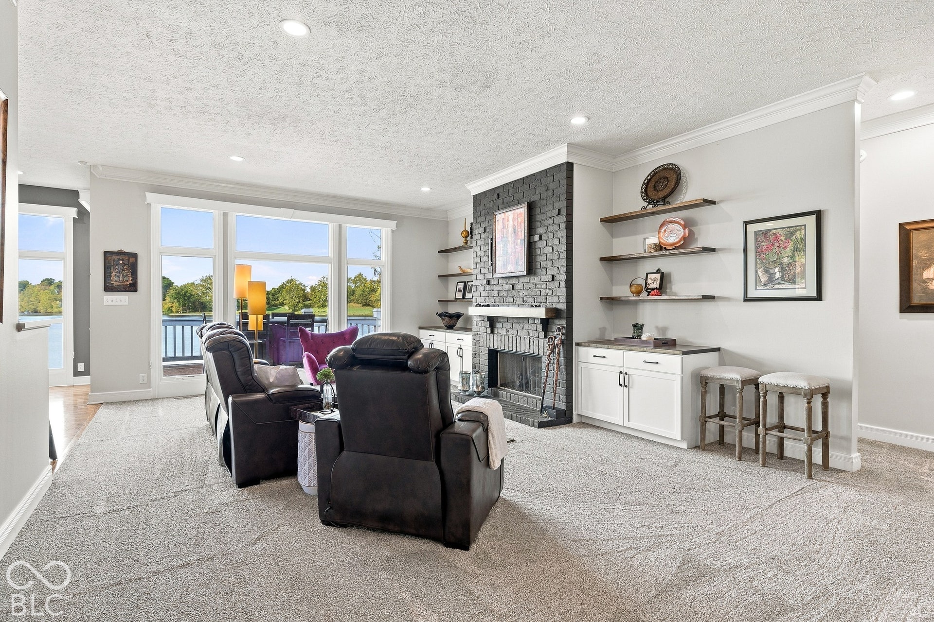 Fireplace with a floor-to-ceiling brick surround, custom built-in cabinetry with shelving, expansive windows, recessed lighting, and crown molding