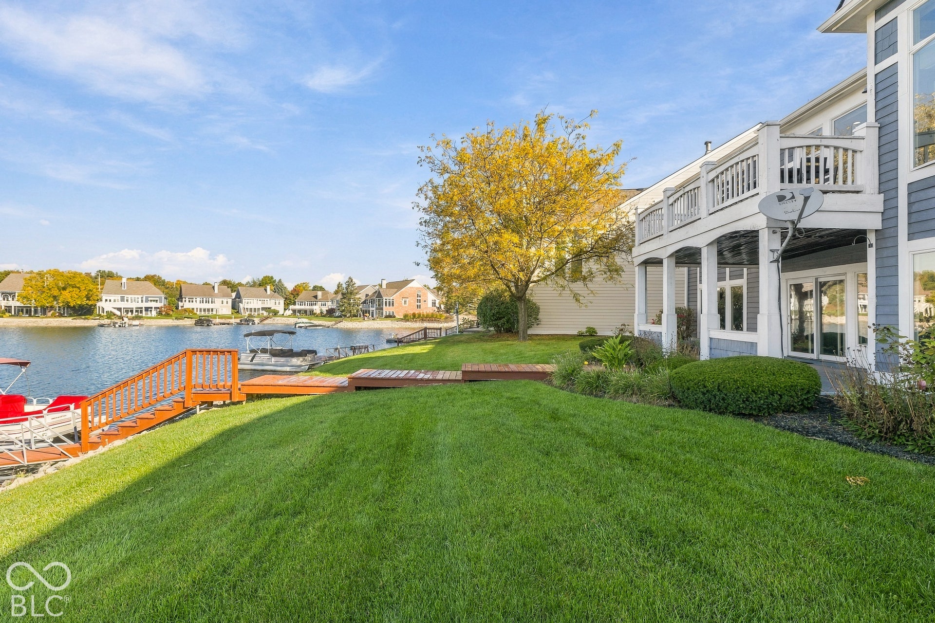 Waterfront backyard featuring a manicured lawn, multi-level wood deck, private wooden dock, and an elevated balcony
