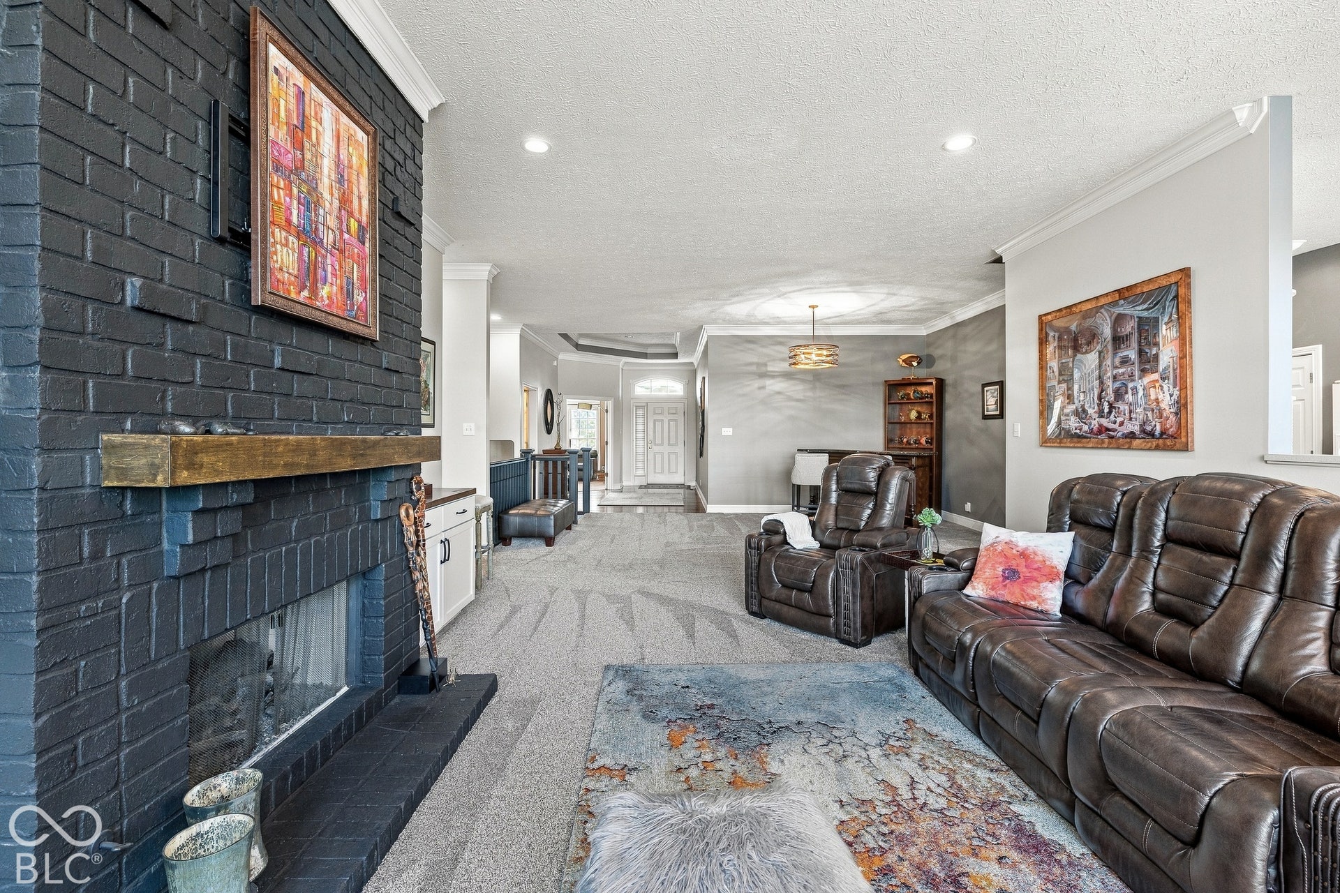 Painted brick fireplace with a wood mantel, crown molding, recessed lighting, and textured wall finish