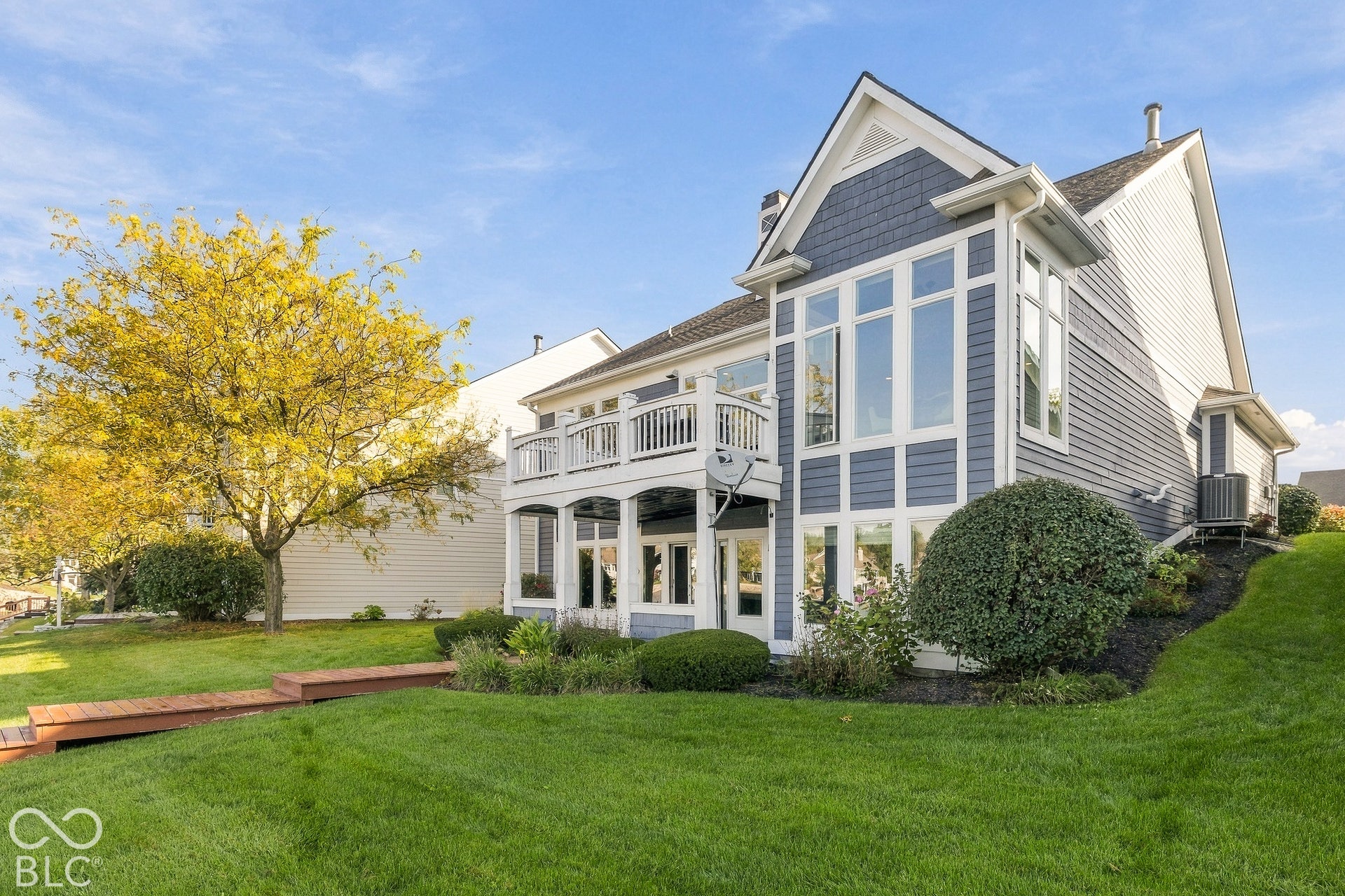 Two-story residence featuring lap siding, shake-shingle accents, an elevated upper-level balcony, a covered lower-level patio, and oversized multi-pane windows