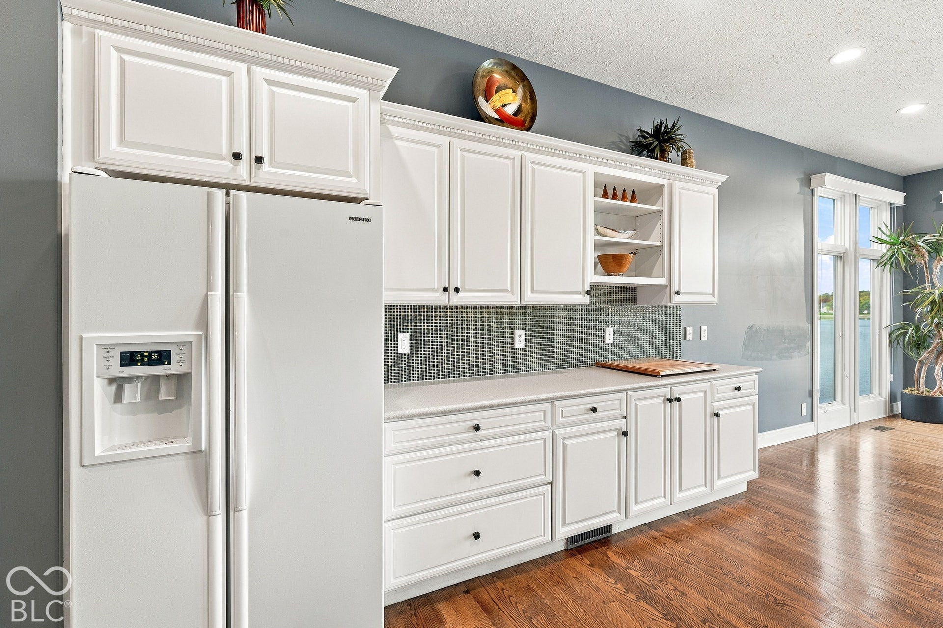 Kitchen featuring white cabinetry with crown molding, integrated open shelving, stone-finish countertops, decorative mosaic tile backsplash, and wood-finish flooring