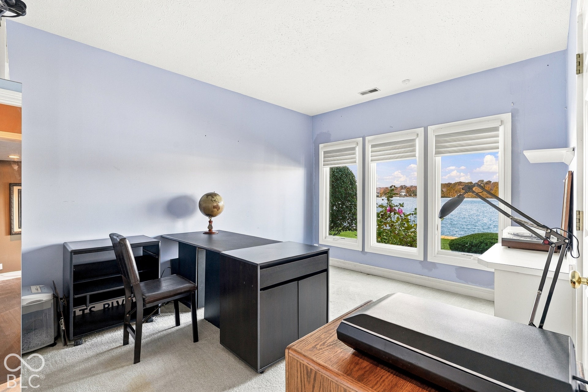 Room featuring neutral carpet, light-toned walls, and a wall of three windows with roller shades providing natural light and exterior water scenery