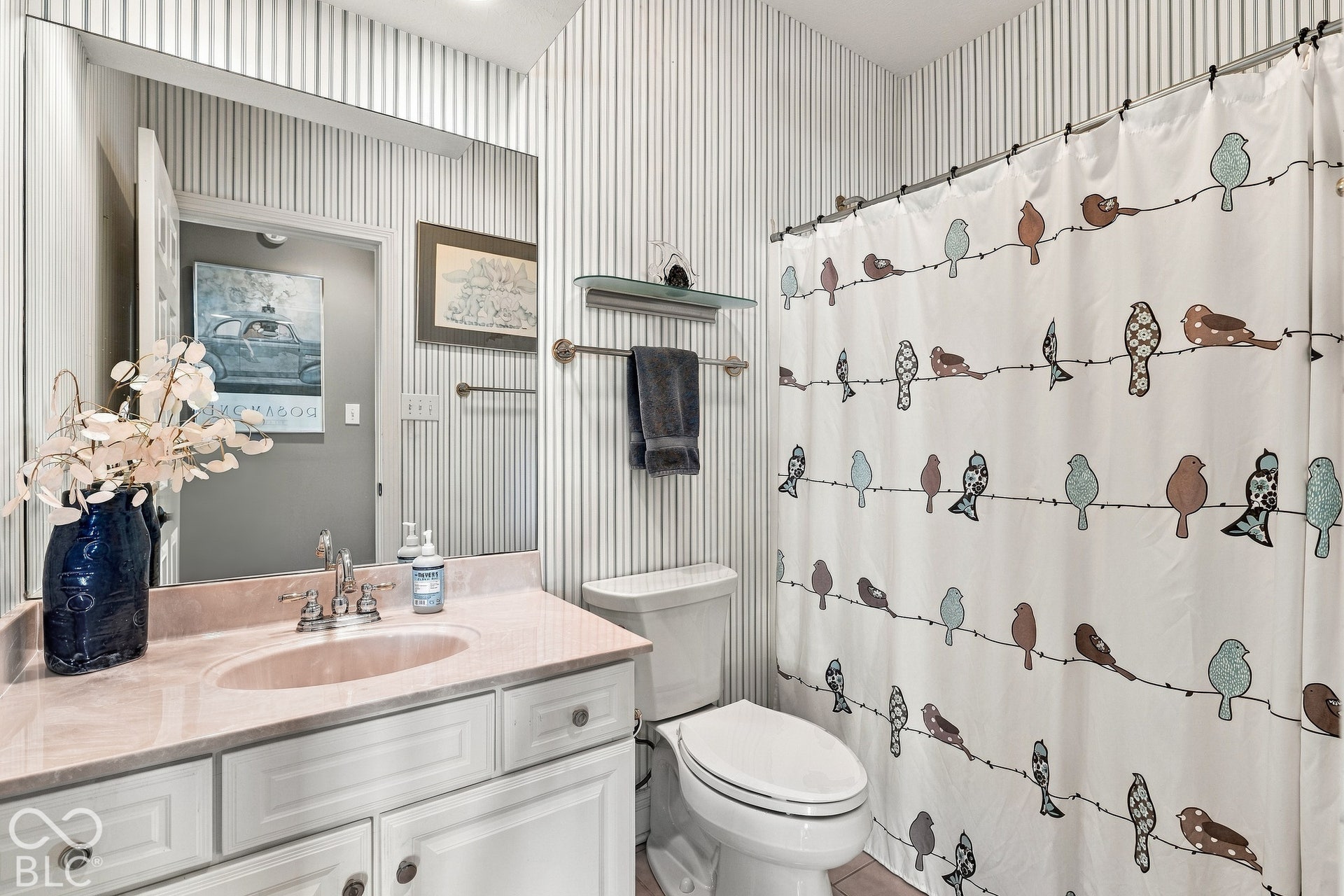 Bathroom featuring a full-width wall mirror, vanity cabinet with an integrated sink and light-toned countertop, and vertical pinstripe wall covering