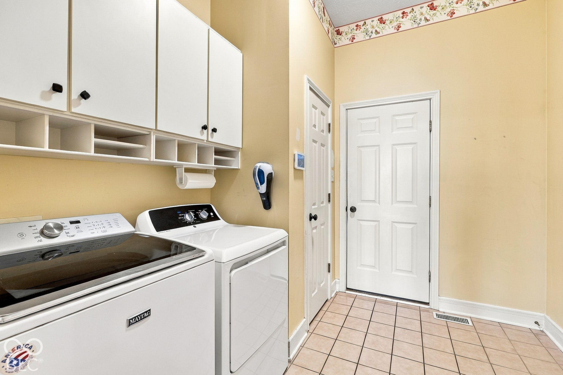 Utility room featuring ceramic tile flooring, white shaker-style cabinetry with open-shelf storage, and a paneled door