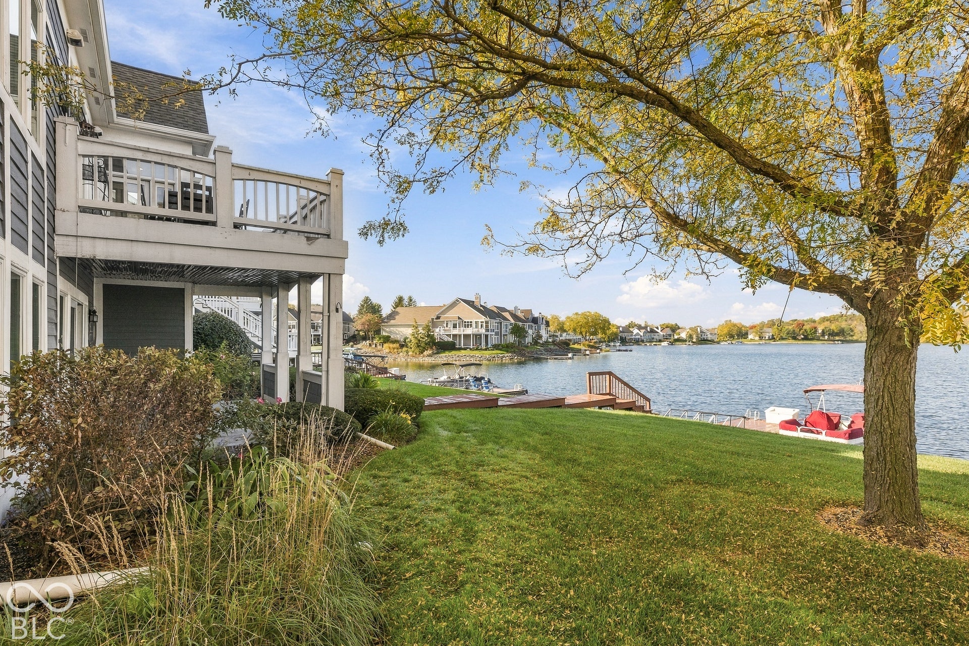 Waterfront residence featuring a private wood-plank dock, multi-level exterior deck, landscaped lawn, and mature canopy trees
